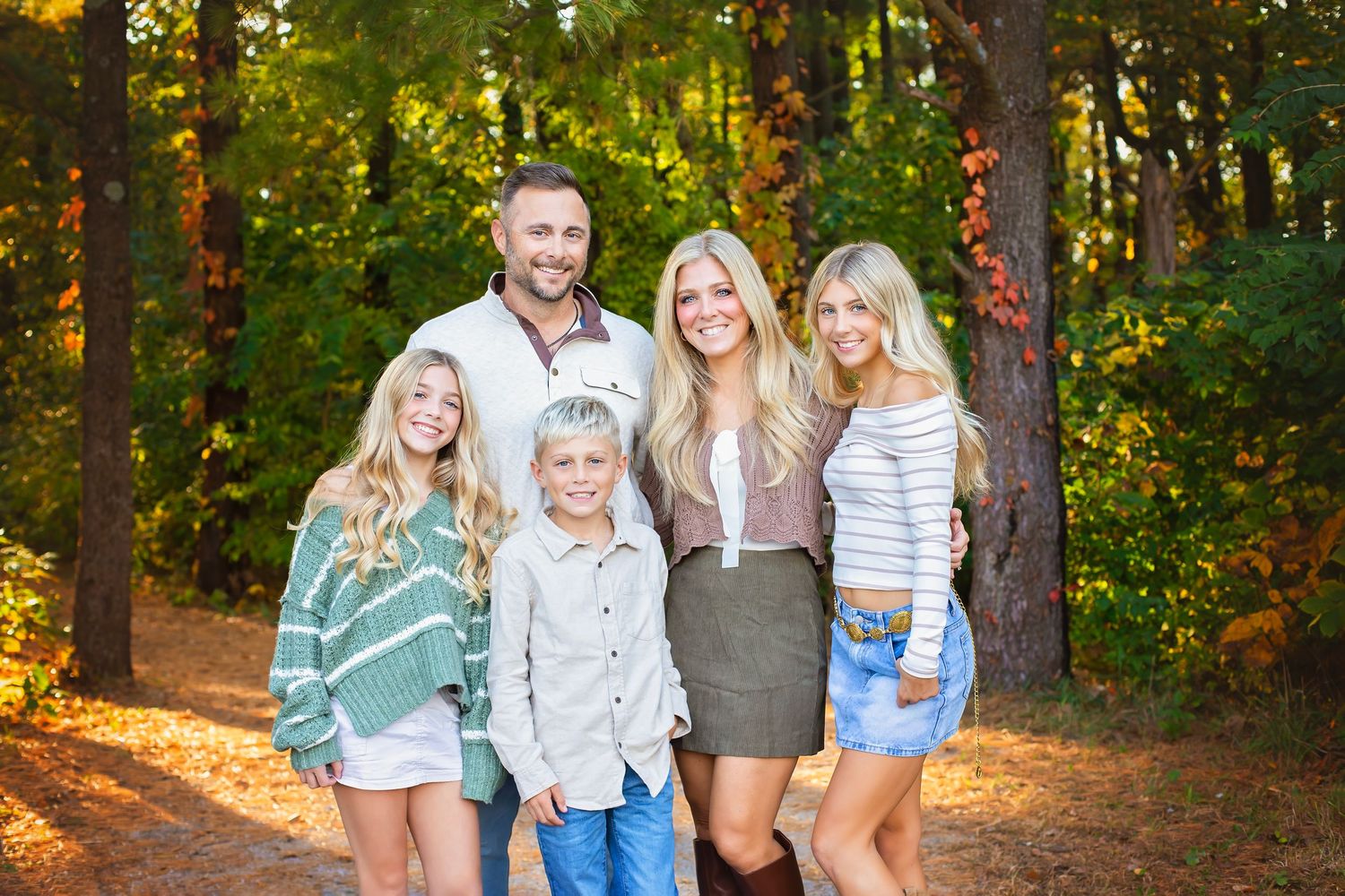 Smiling family of five standing together on a forest path in autumn light.