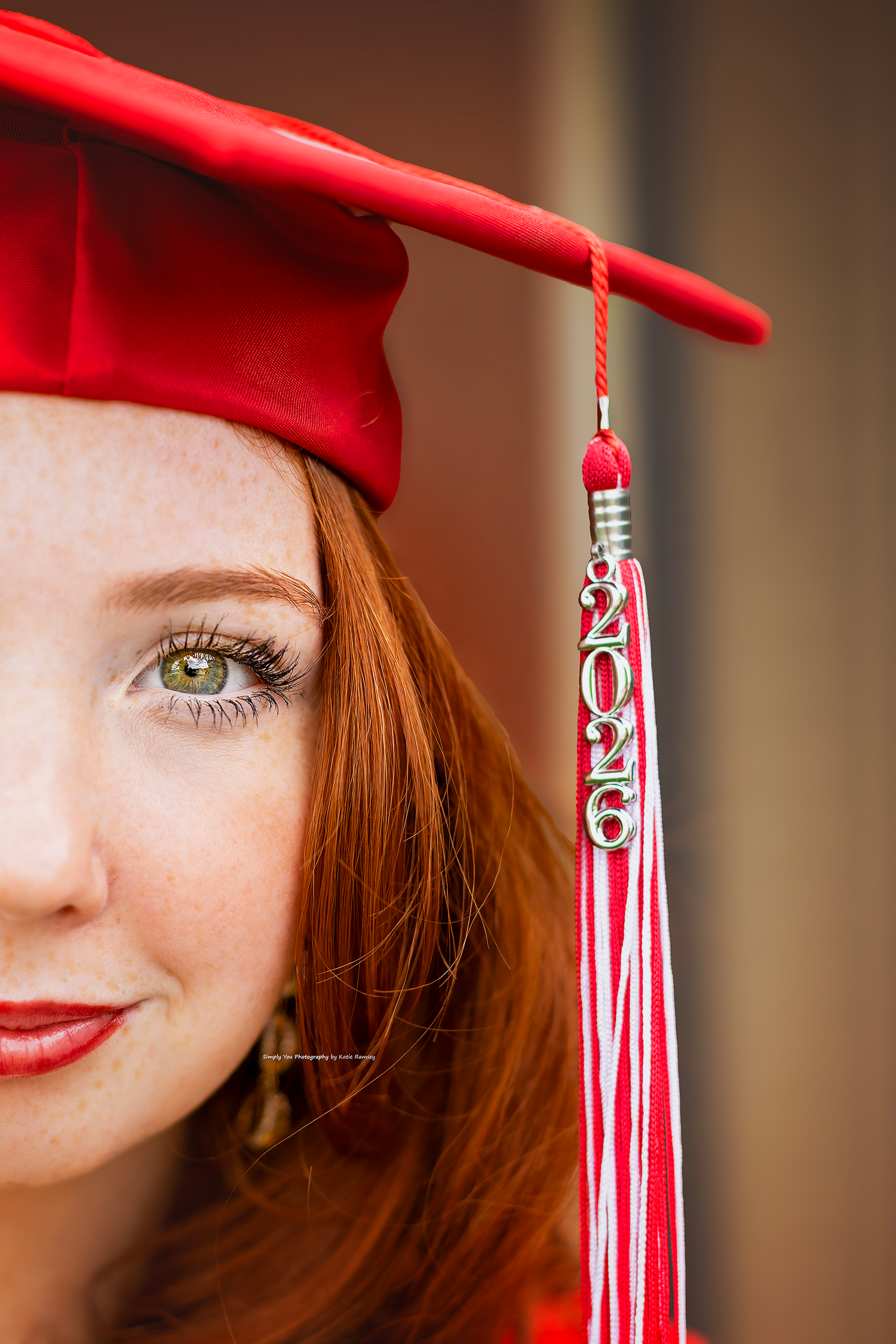 Close-up of a redhead girl in a red graduation cap with a 2026 tassel, showcasing green eyes and freckles.