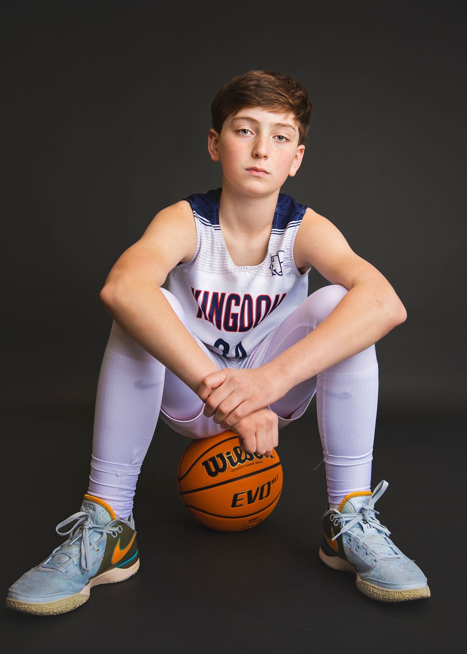 Teen boy in Kangaroos basketball uniform sitting on Wilson ball.