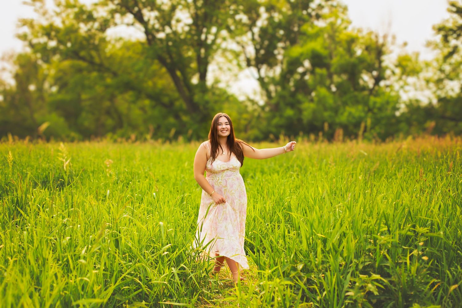 Young woman in floral maxi dress walking through tall green grass field.