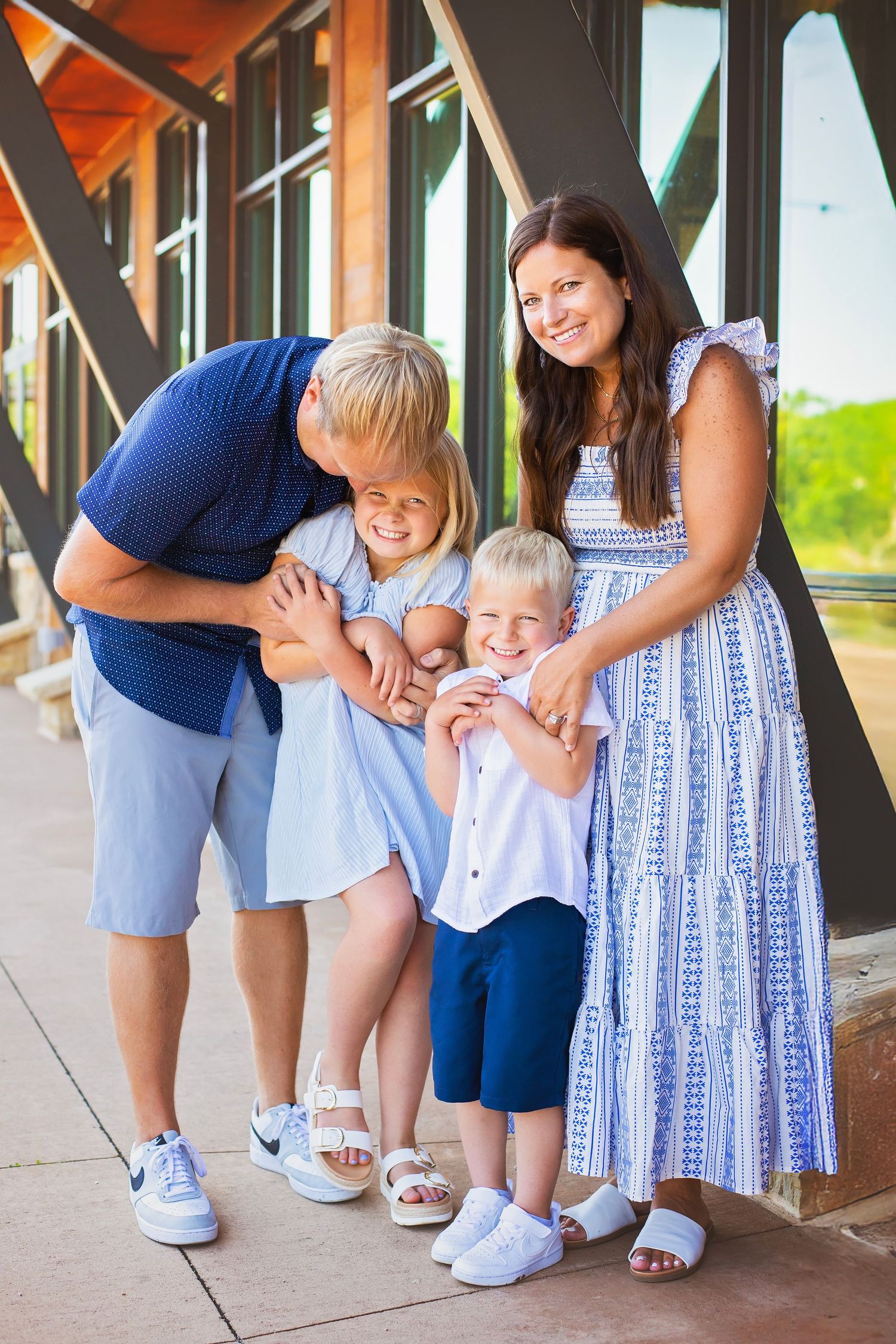 Happy family of four poses together outdoors, parents and two children smiling in coordinating blue outfits.