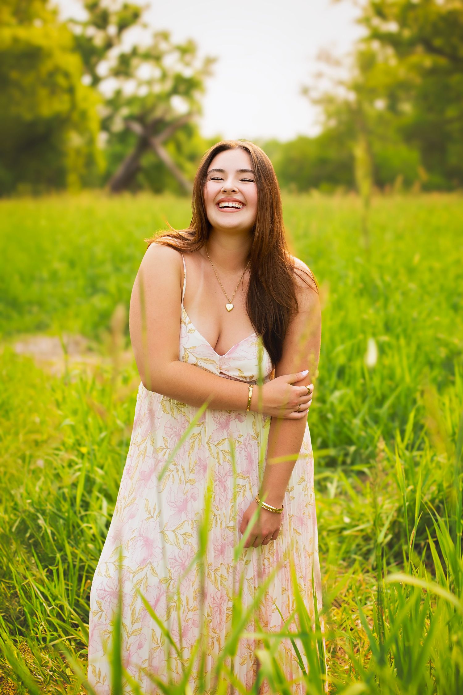 Young woman in floral sundress laughing joyfully in lush green meadow.