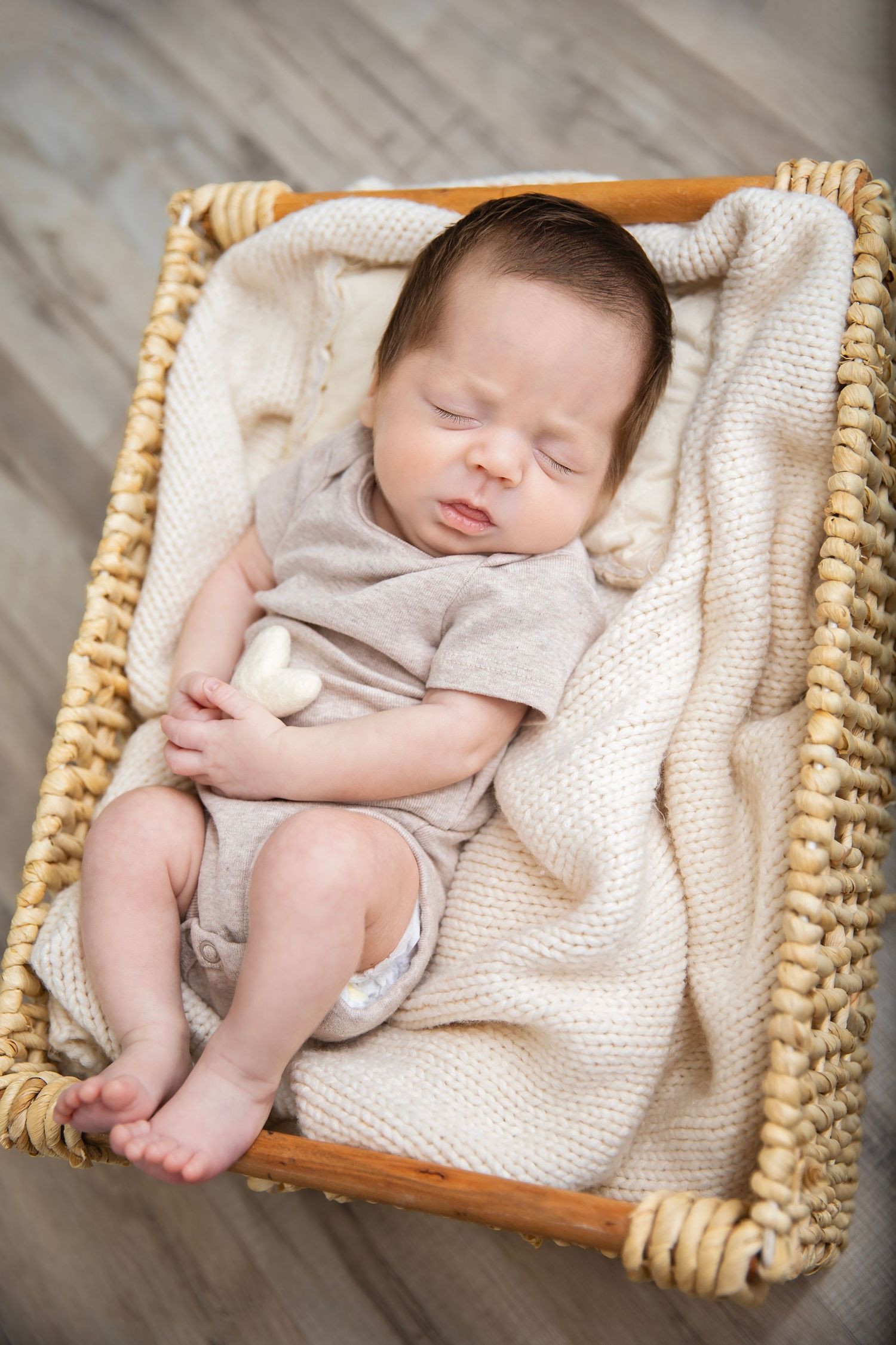 Peaceful newborn baby sleeping in a wicker basket with a soft cream knit blanket.
