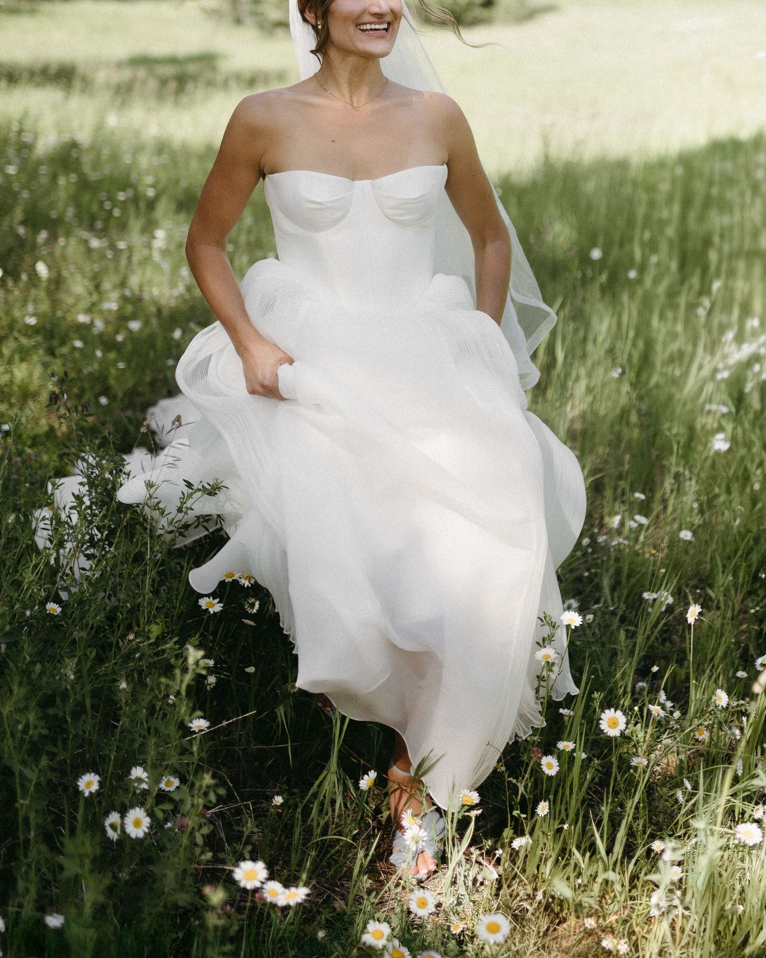 A bride's white dress flows gracefully through a field of delicate wildflowers.