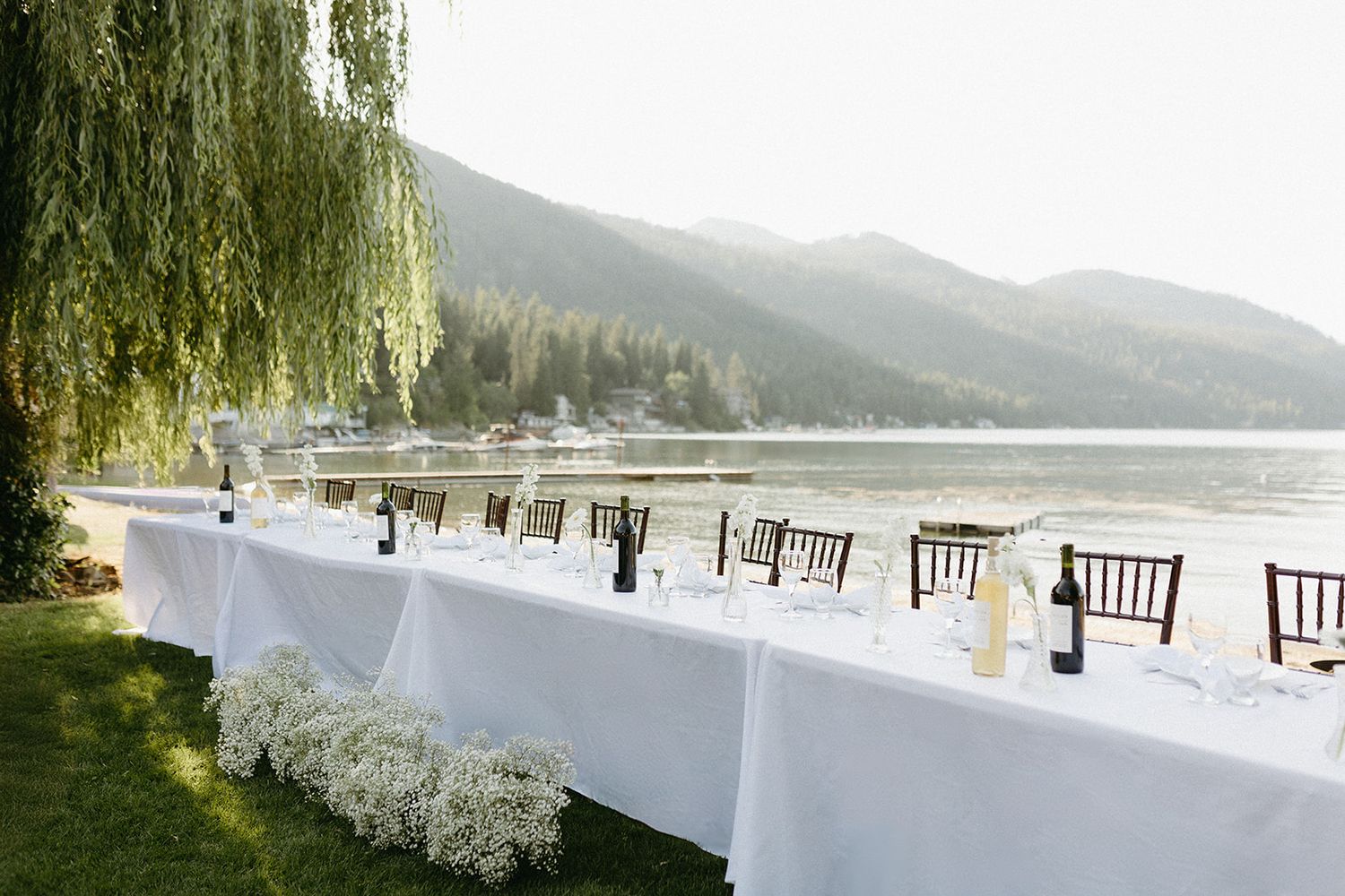 White tablecloths and chairs set up for outdoor wedding reception by a lakeside.