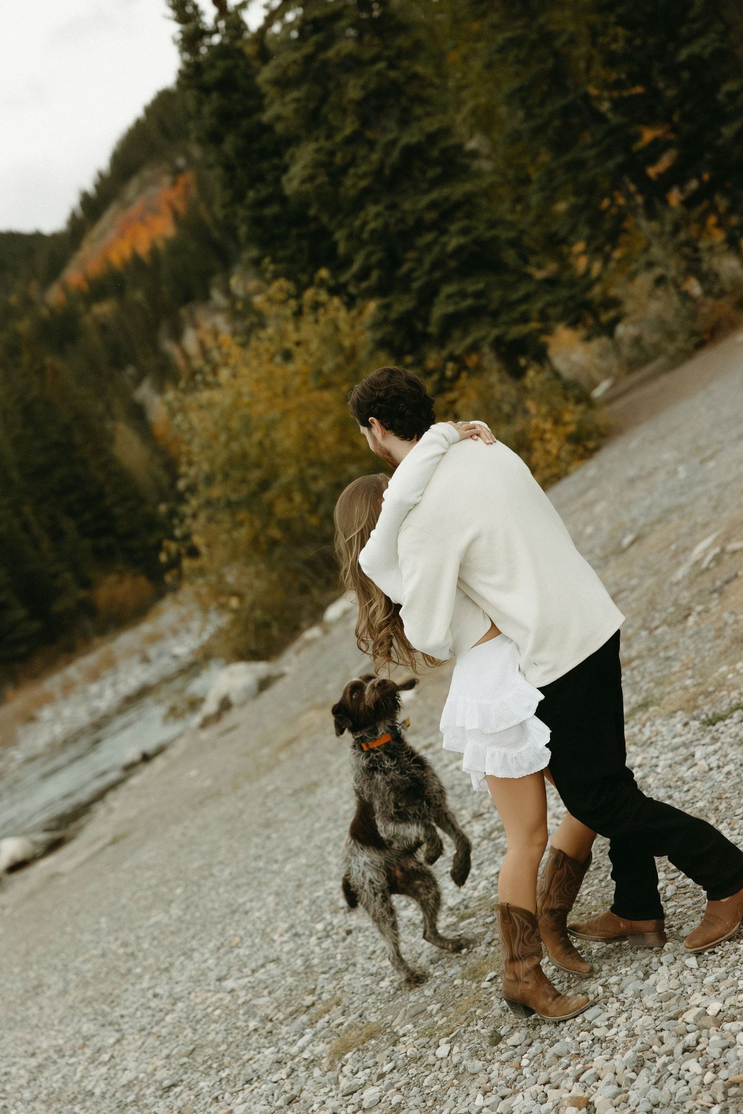 A couple plays with their energetic dog on a rocky mountain shore.