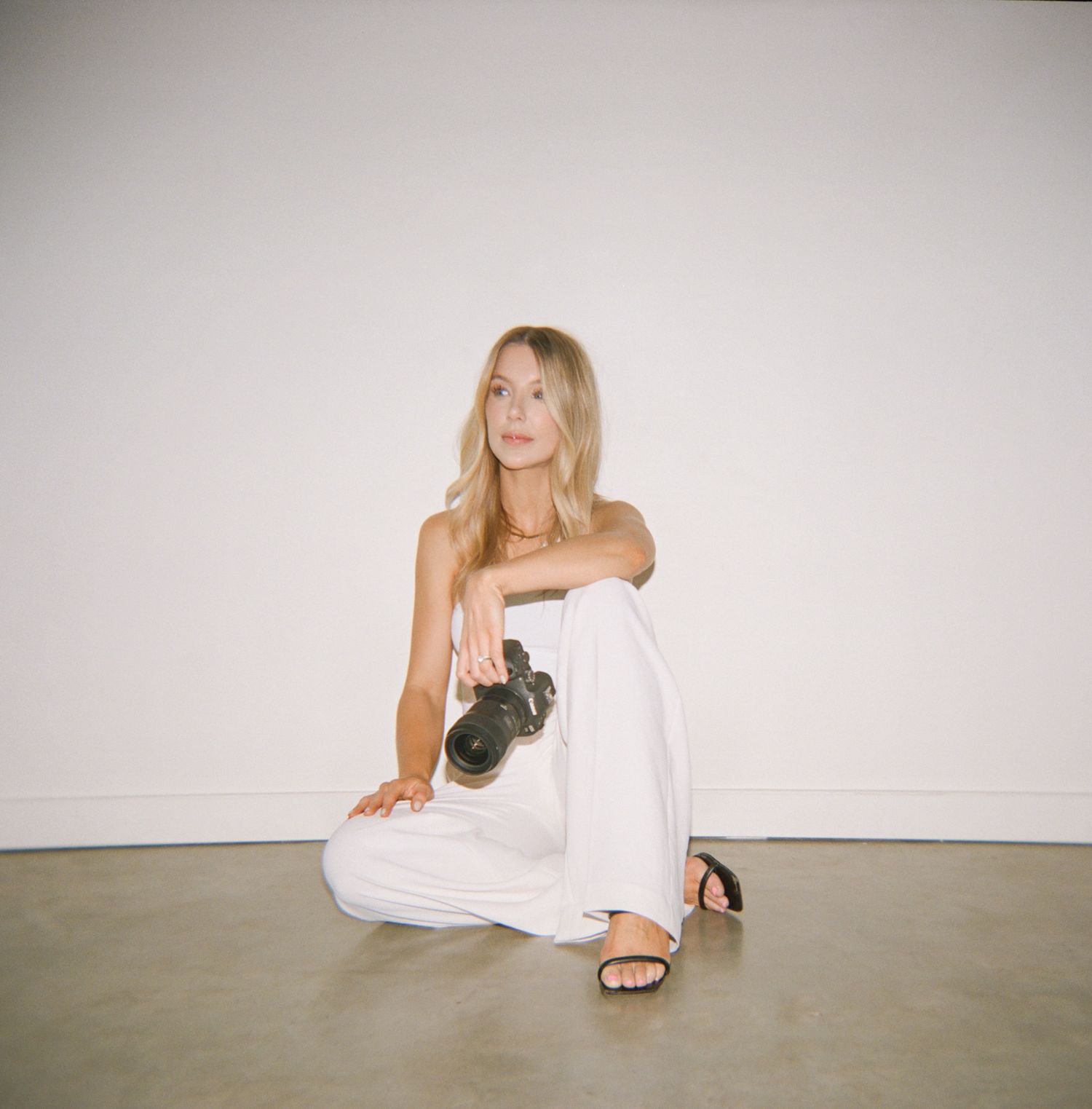 Person in white dress sitting on concrete floor with camera.