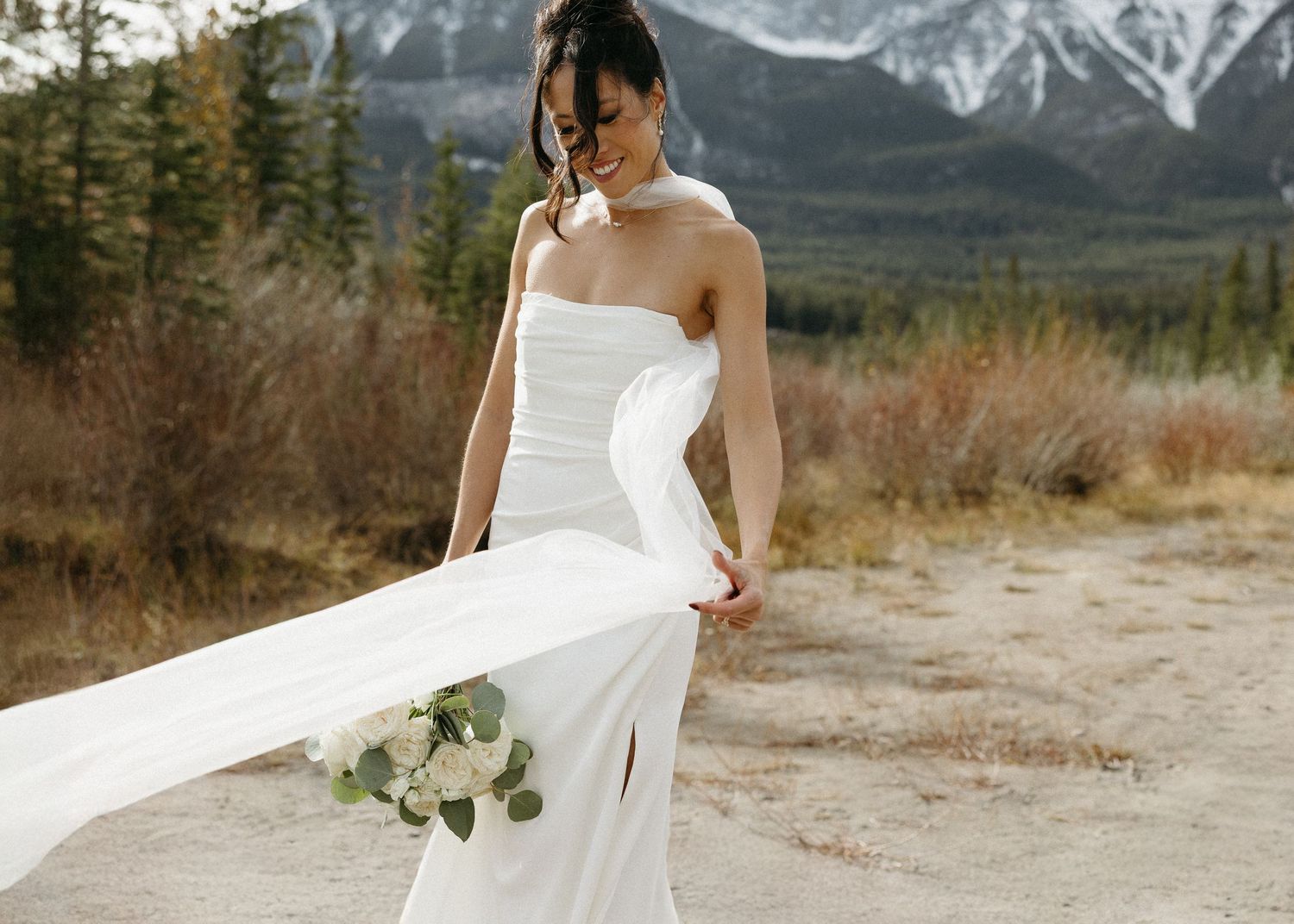 Flowing white wedding dress captured against dramatic mountain landscape.