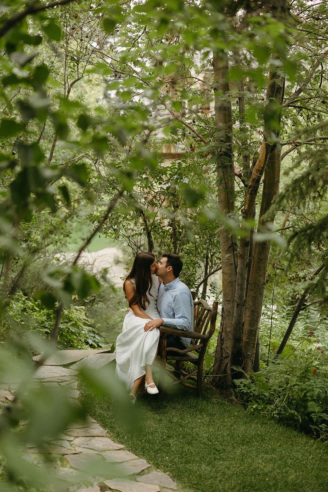 Romantic moment captured between couple on wooded path surrounded by lush greenery.