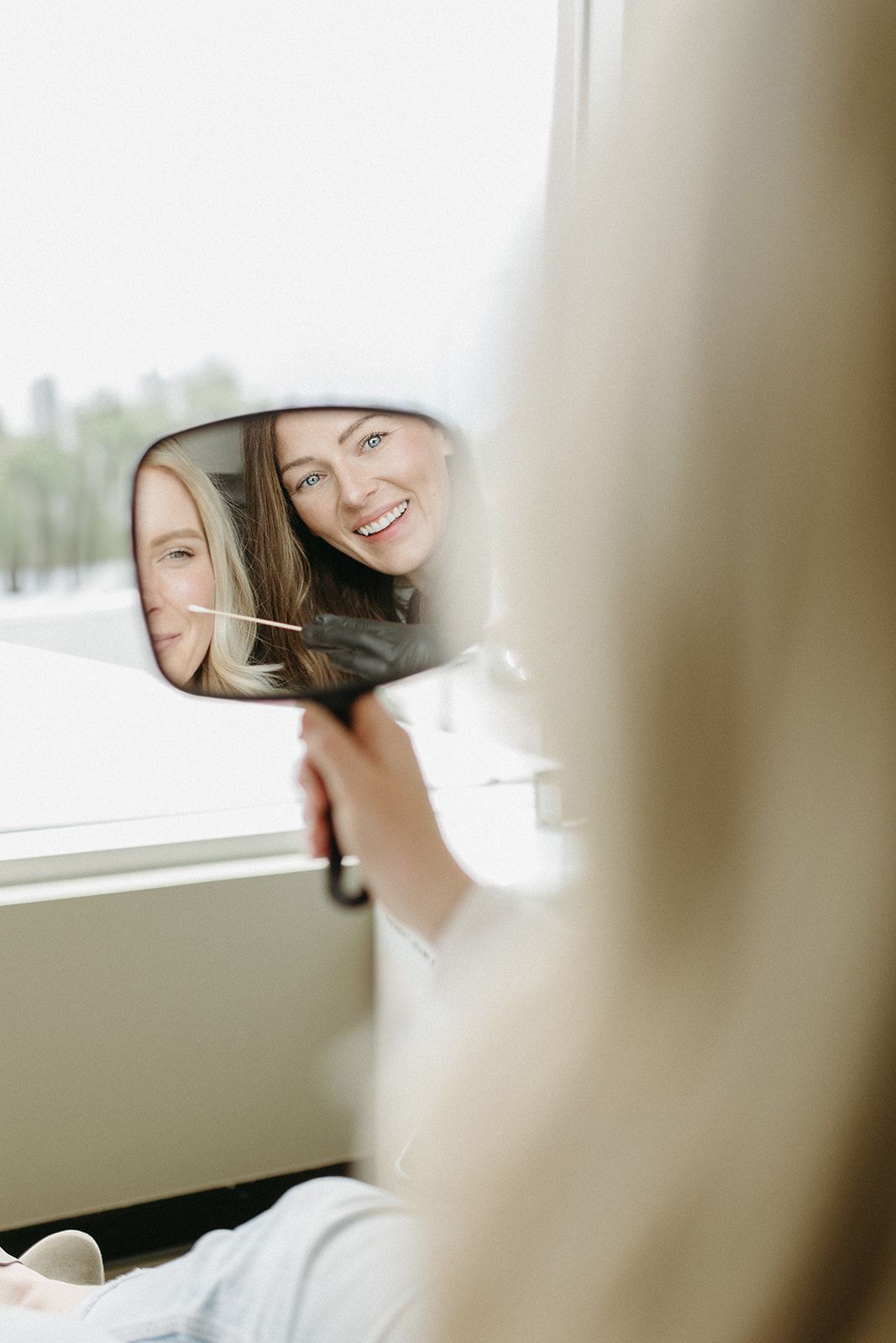 Reflection in car side mirror shows two people smiling together on a bright day.