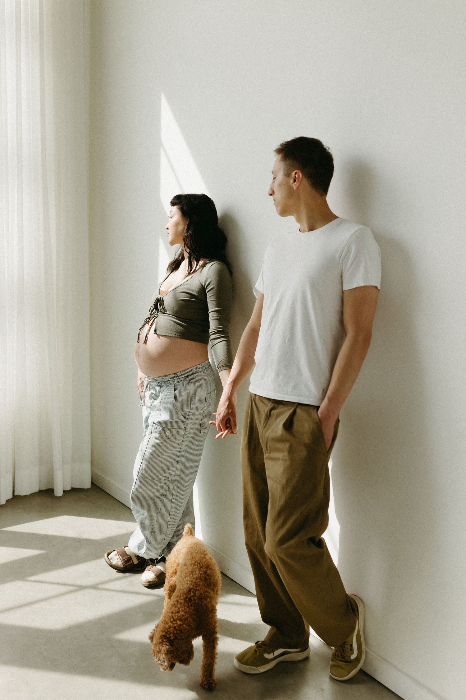 Two people and a brown dog stand by a window in a bright minimalist space.