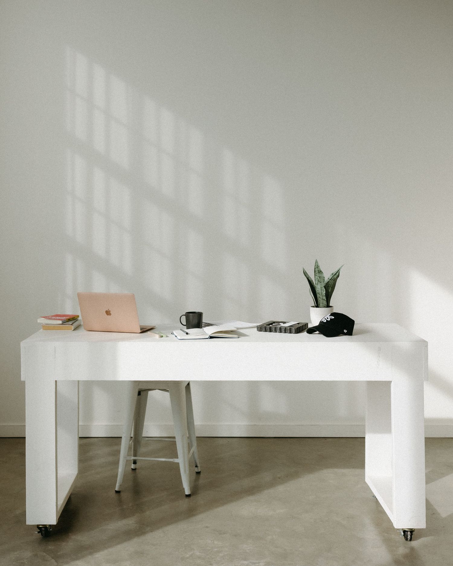 Modern minimalist white room with concrete floors and sunlight casting geometric shadows.