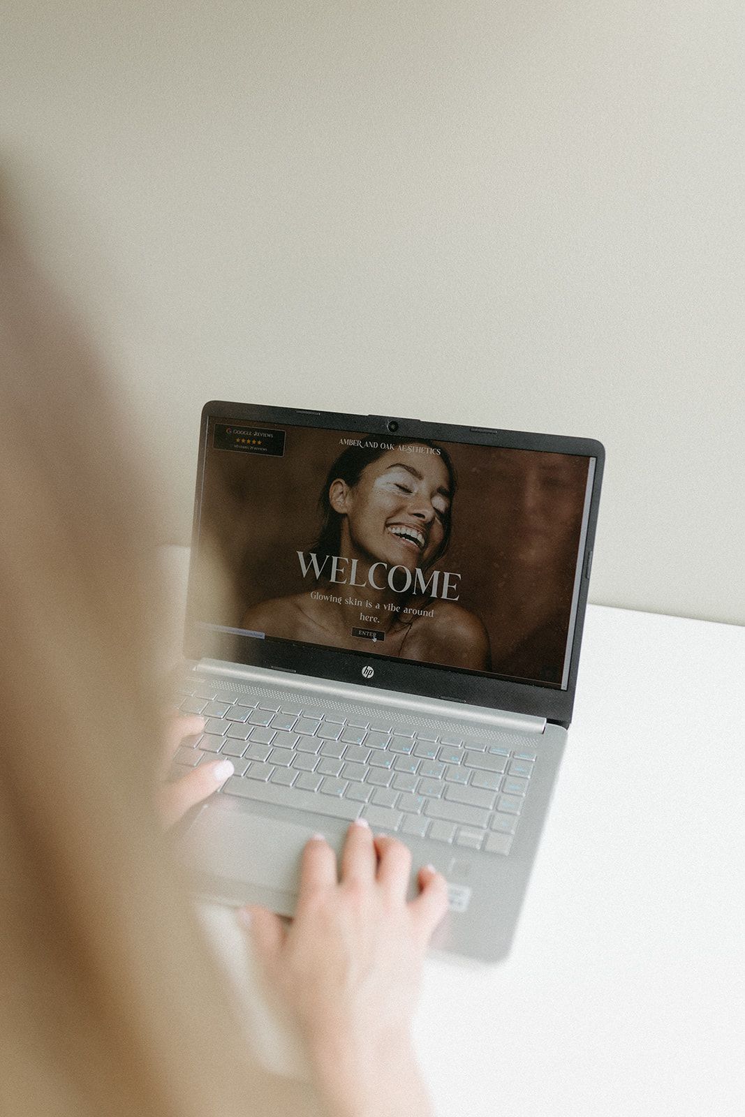 Hands typing on white laptop keyboard with website welcome screen visible.
