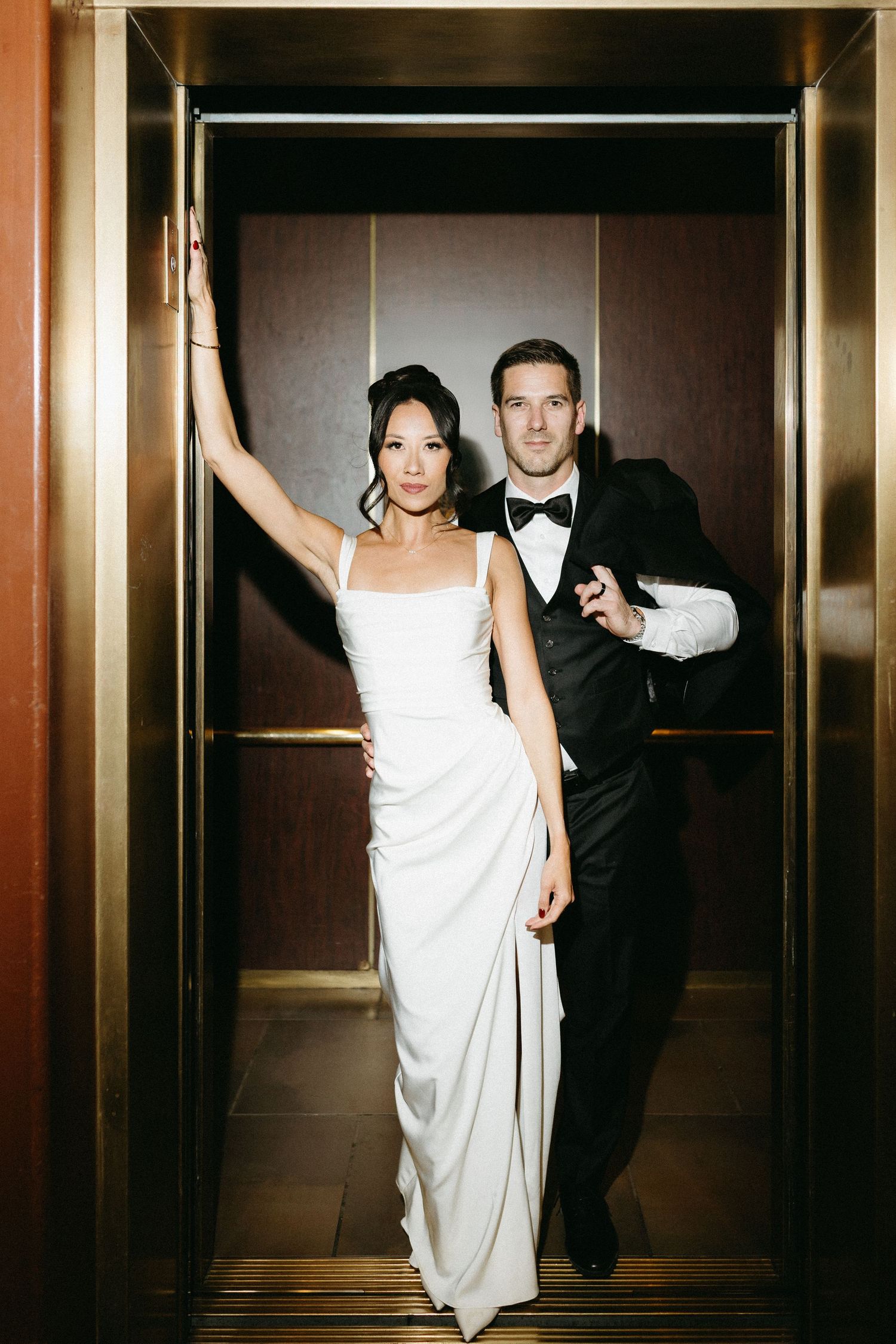 Stylish bride and groom posing playfully in modern elevator with gold accents.