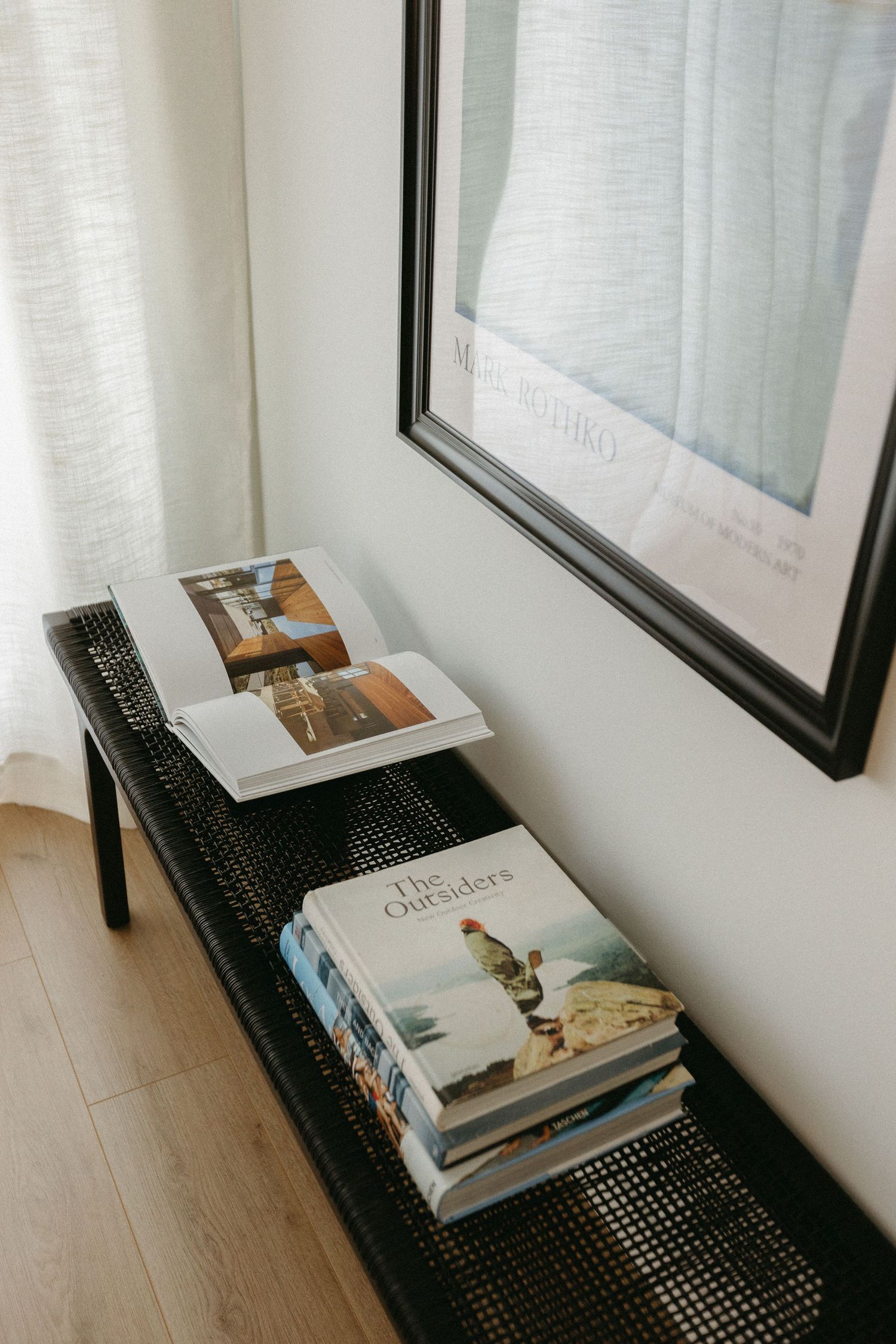 Books and magazines displayed on a black mesh shelf against a white wall.