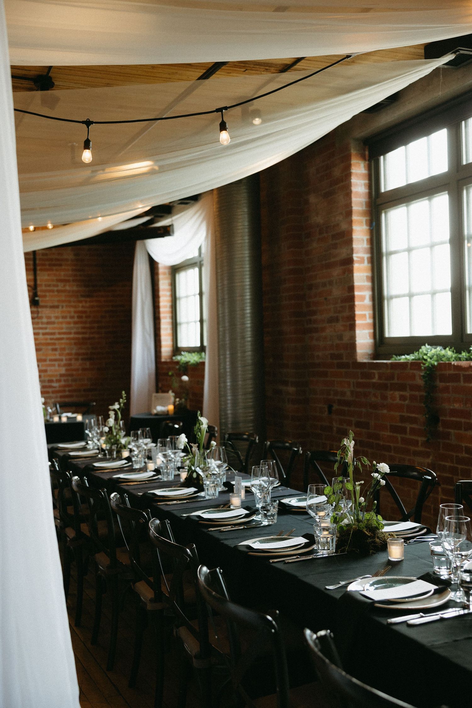 Modern industrial wedding reception venue with exposed brick and white draping decorations.