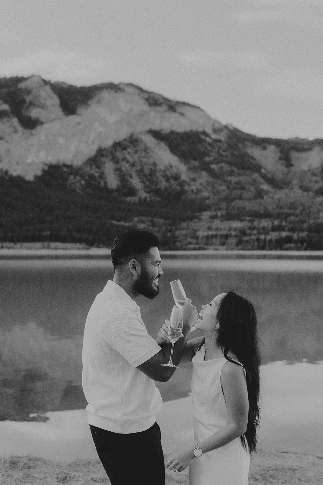 Couple sharing drinks by a scenic mountain lake in black and white photography.