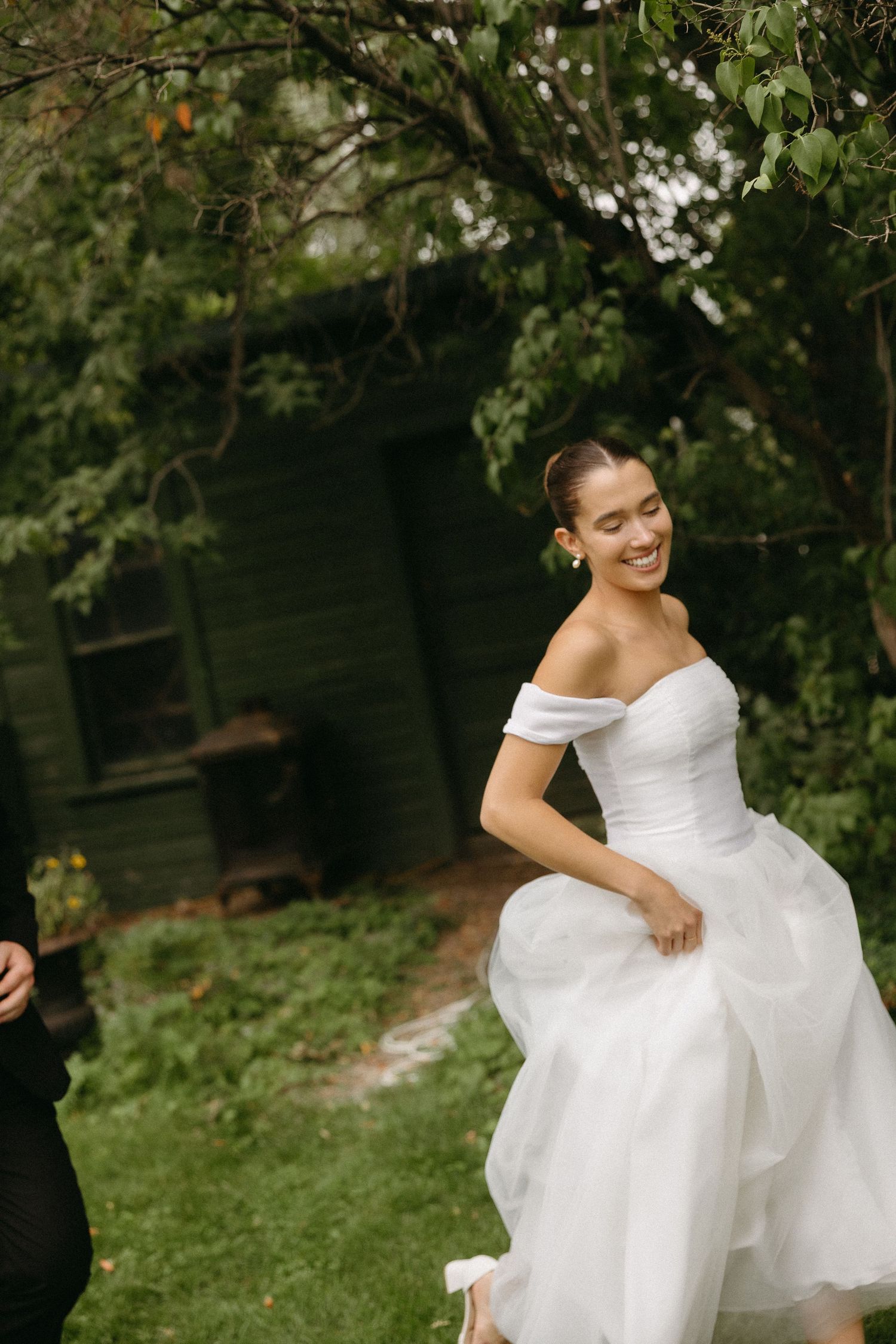 A person in a flowing white wedding dress twirls gracefully in a lush garden setting.