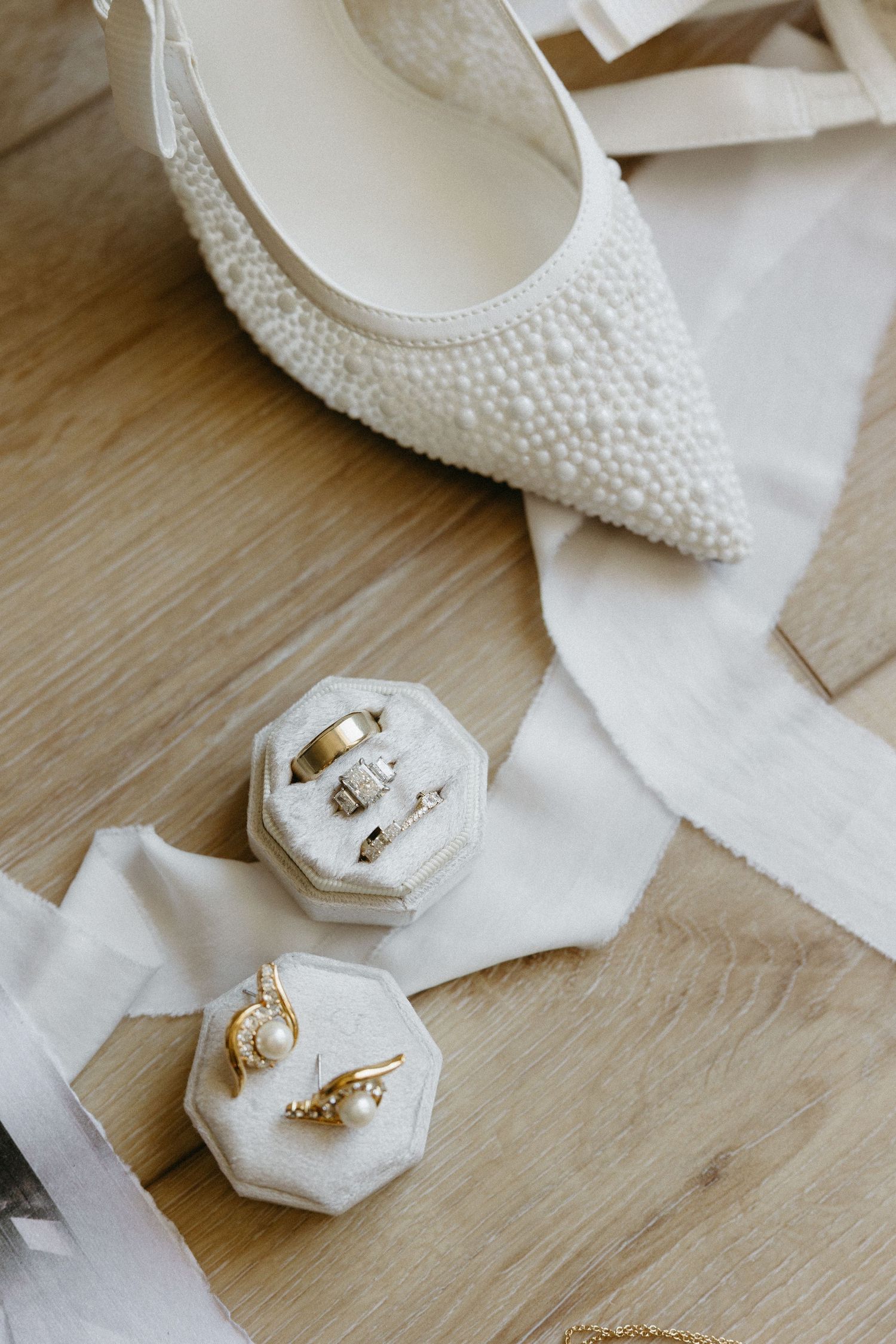 Pearl-embellished bridal shoes with wedding rings in hexagonal boxes on wooden floor.