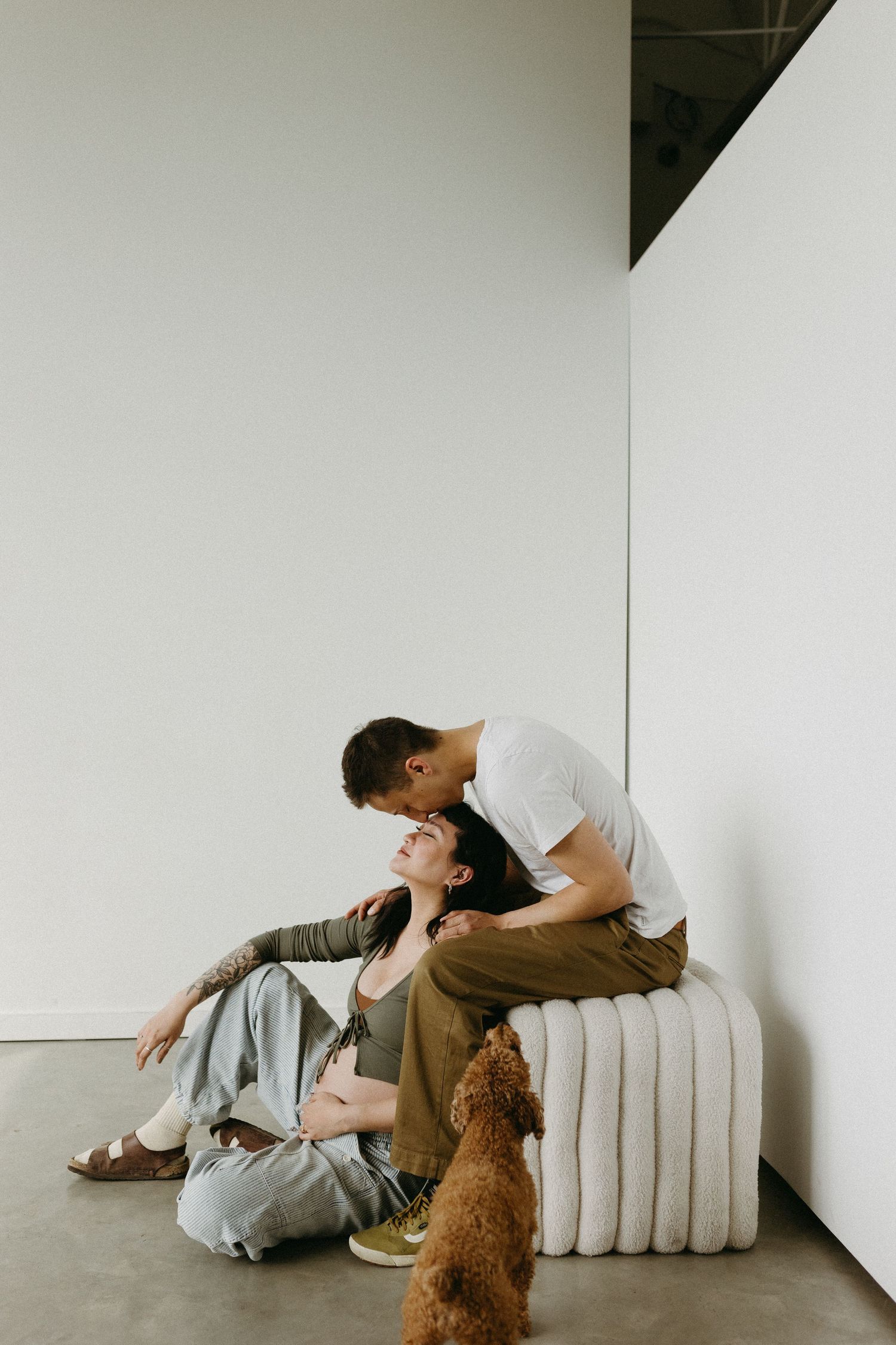 A couple relaxes on a white couch with their brown dog in a bright, airy room.