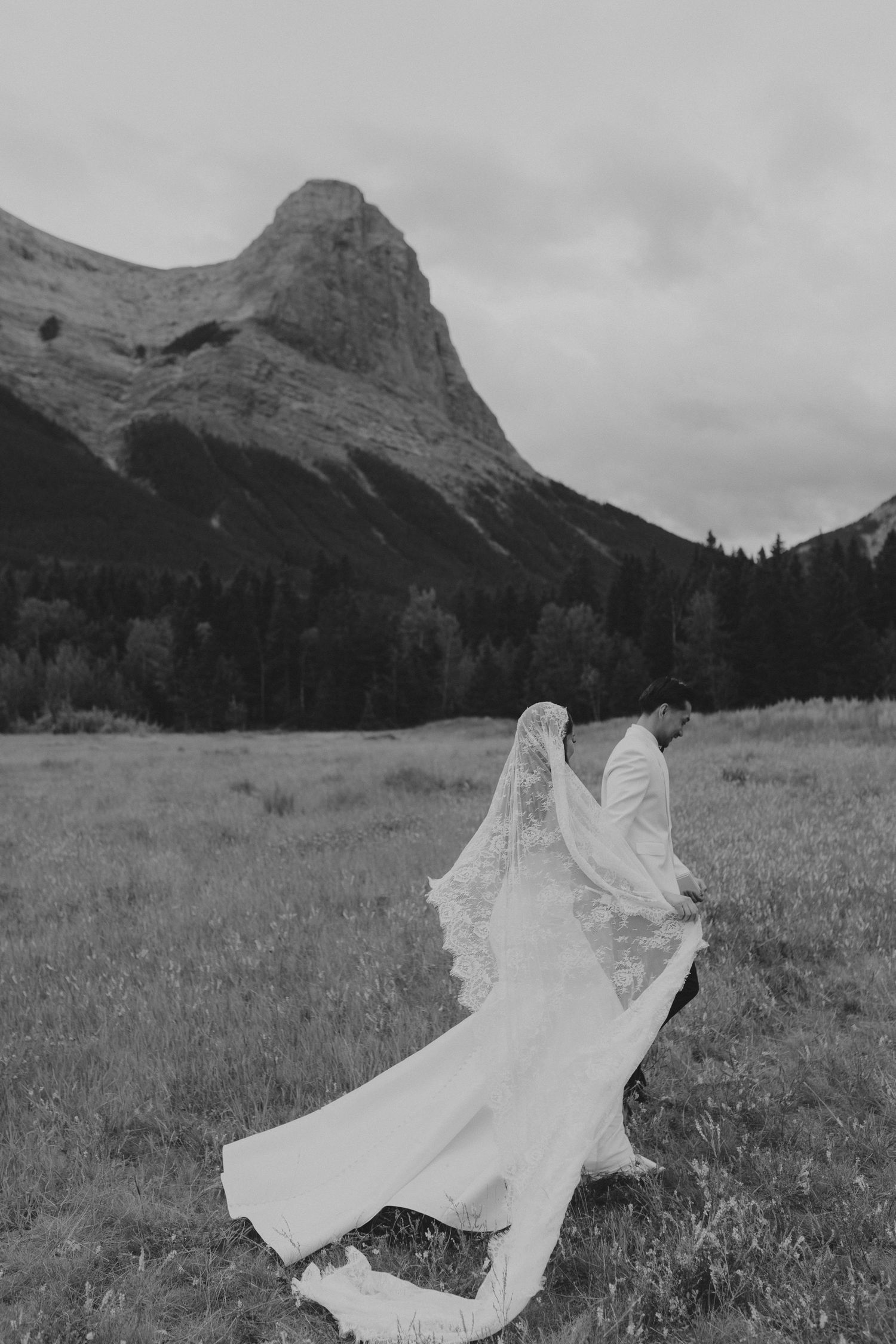 Black and white photos of flowing wedding dress in mountain meadow.