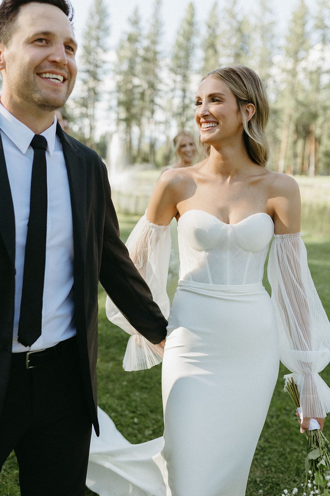Newlyweds share joyful moments in a sunlit forest setting wearing classic wedding attire.