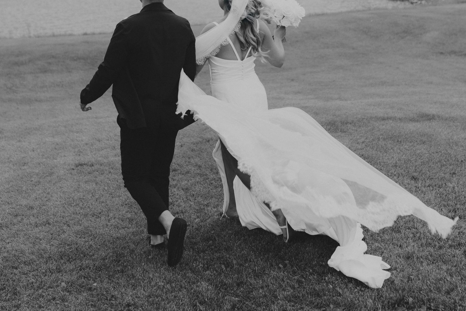 A black and white wedding photo captures flowing dress movement across a grassy field.