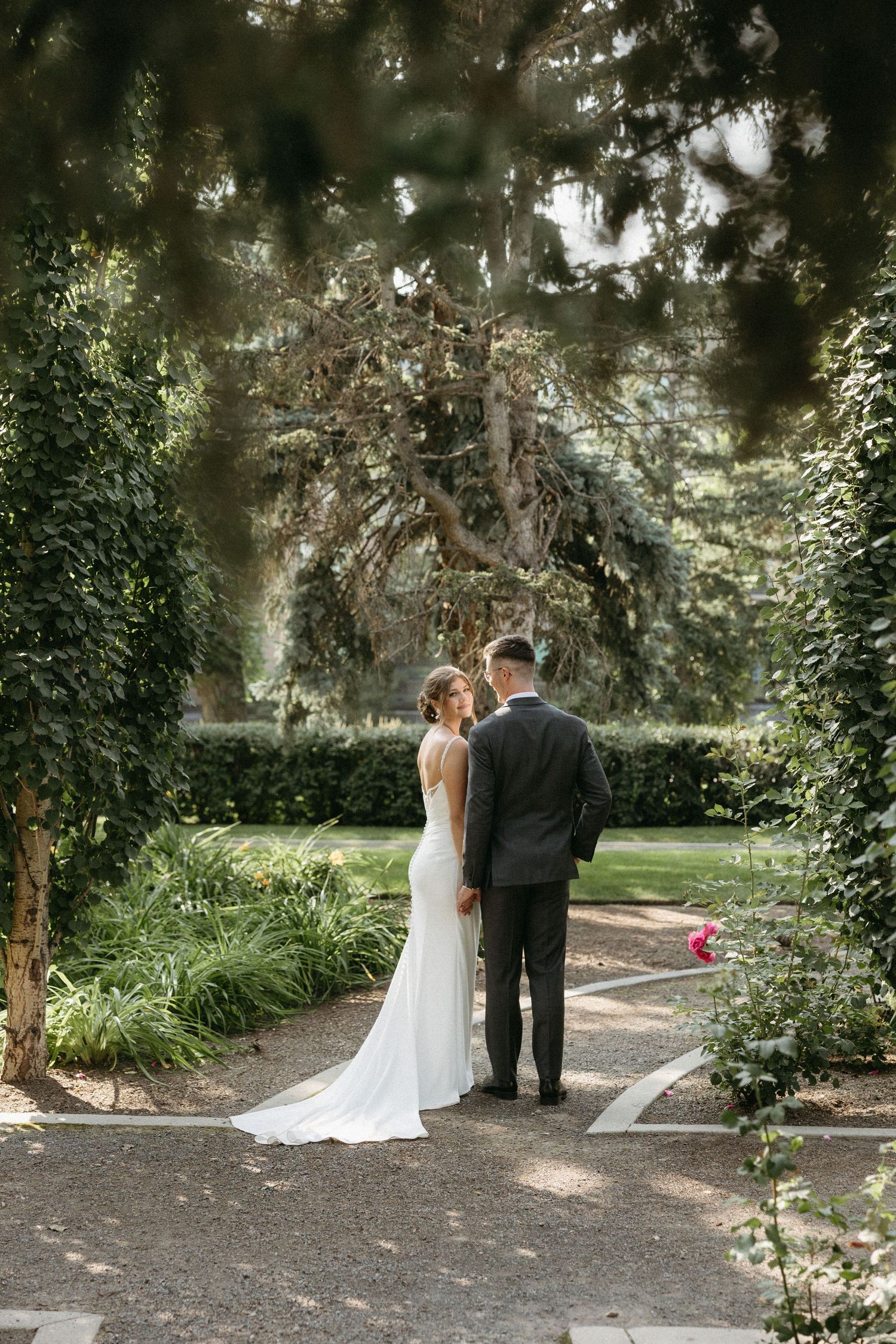 A couple in wedding attire shares an intimate moment together in a lush garden setting with overhanging trees.