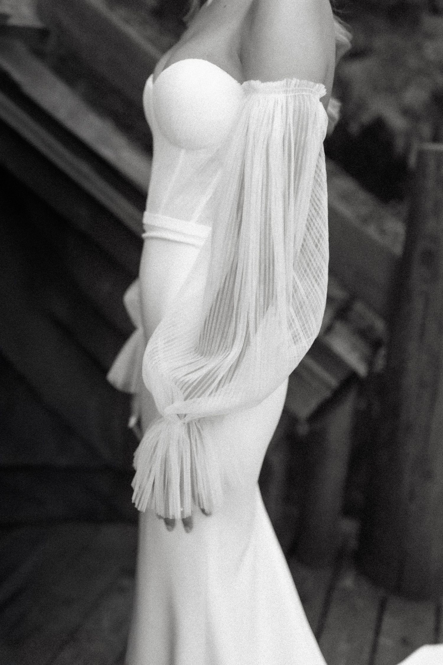 A white strapless wedding gown with flowing draped sleeves and a fitted mermaid silhouette is displayed in black and white.