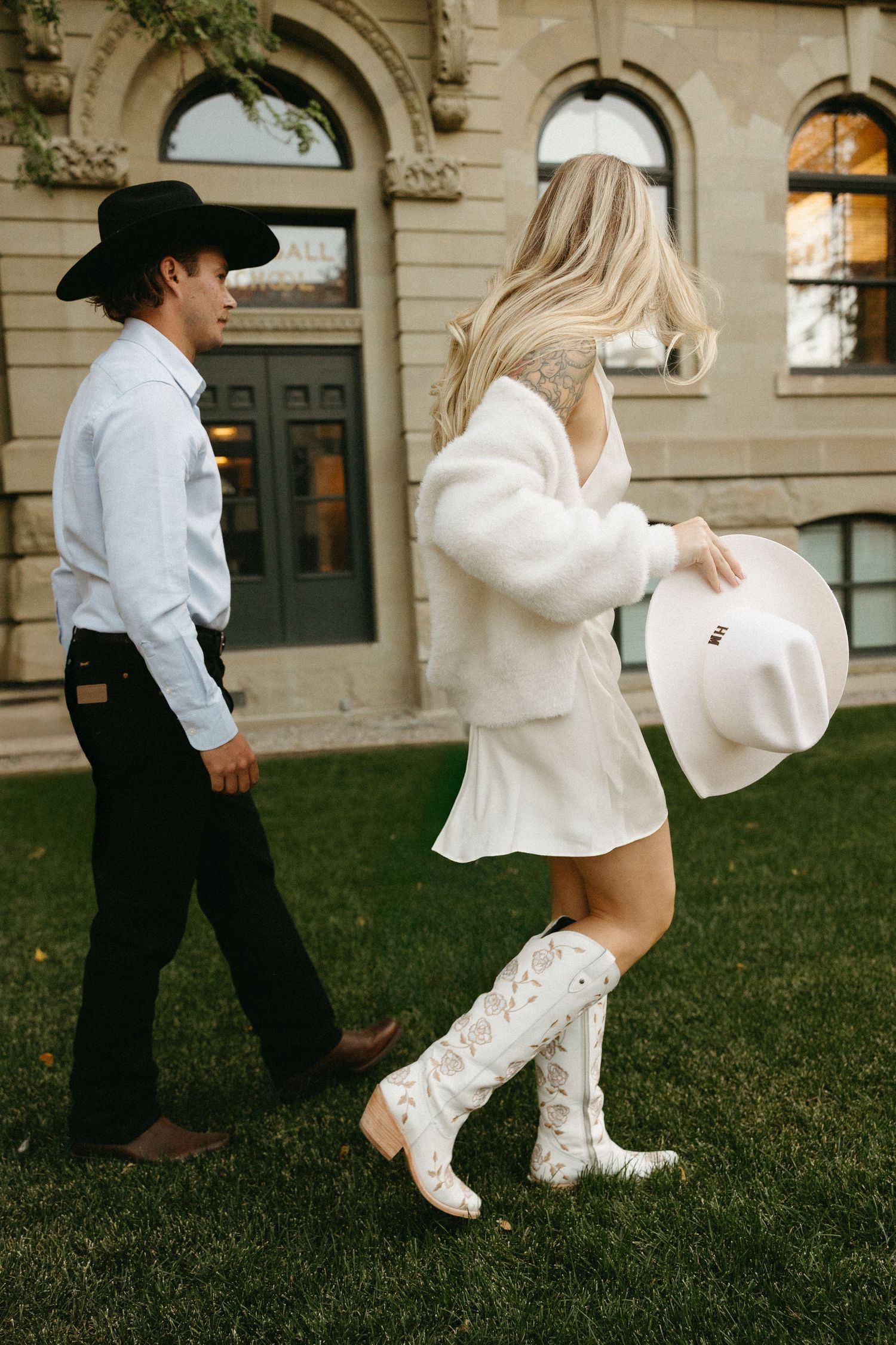 Dancing couple in western attire twirls on grass near a classical building facade.