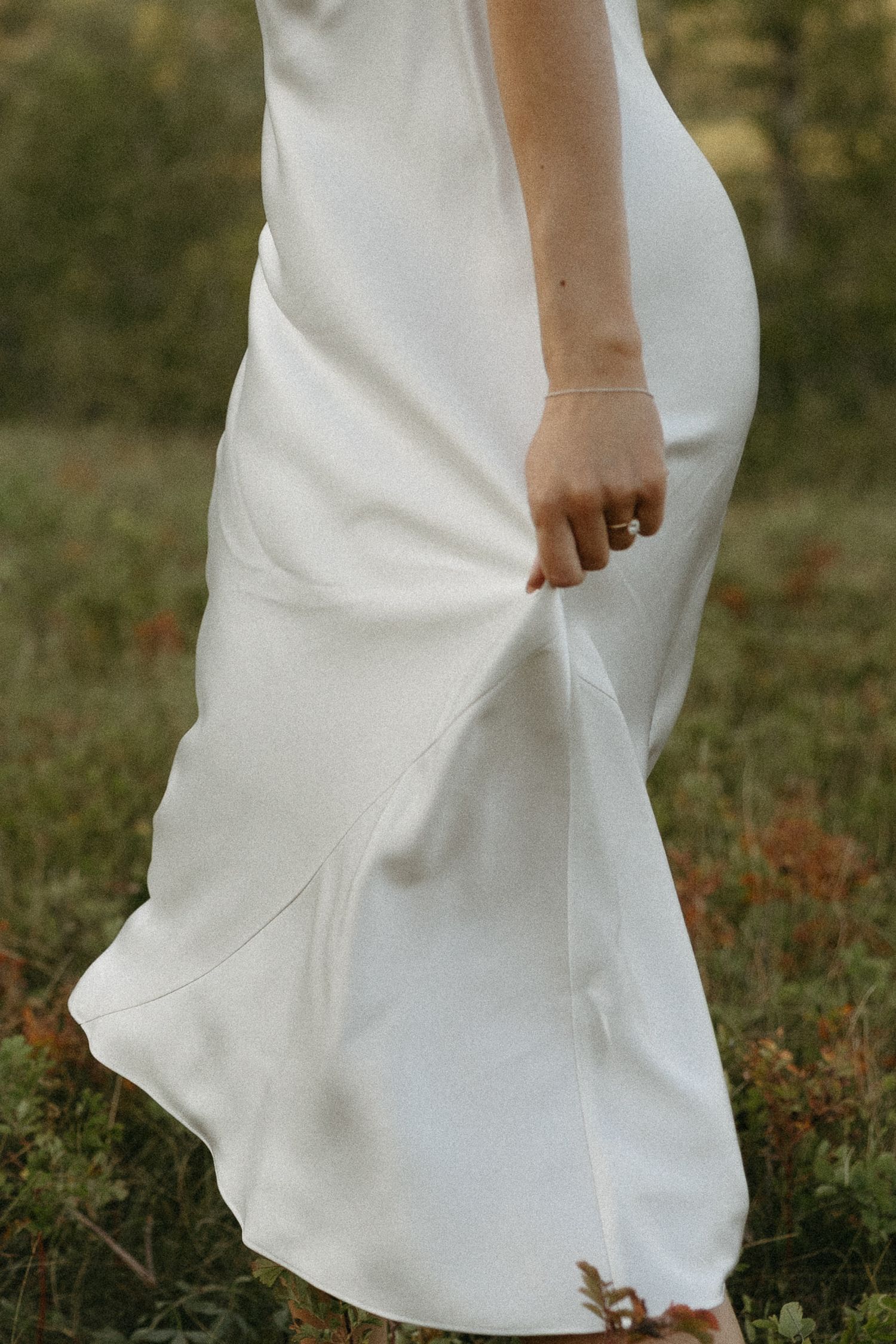 Close-up details of a flowing white dress against grassy field backdrop.