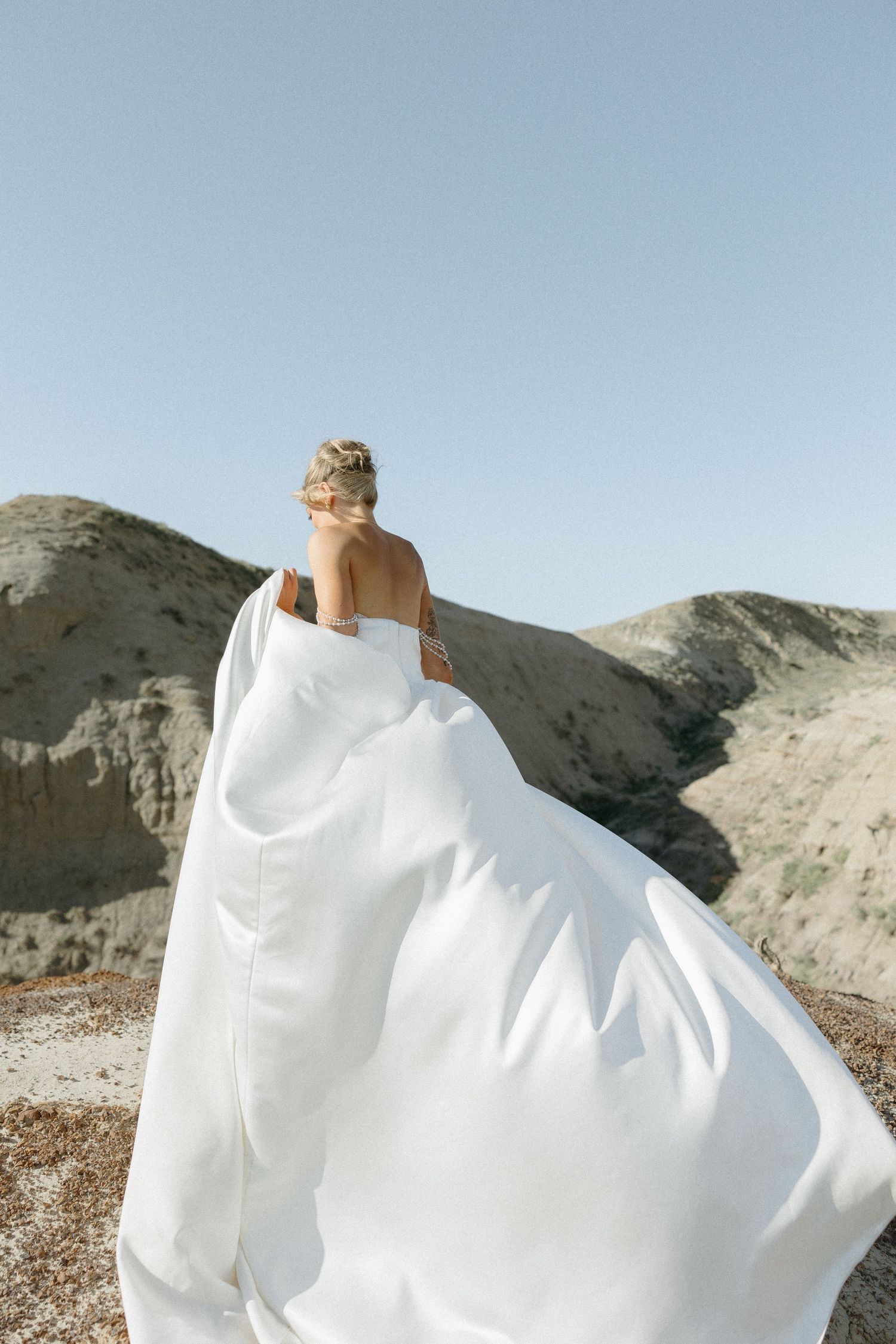 Flowing white wedding dress billows dramatically against desert landscape.