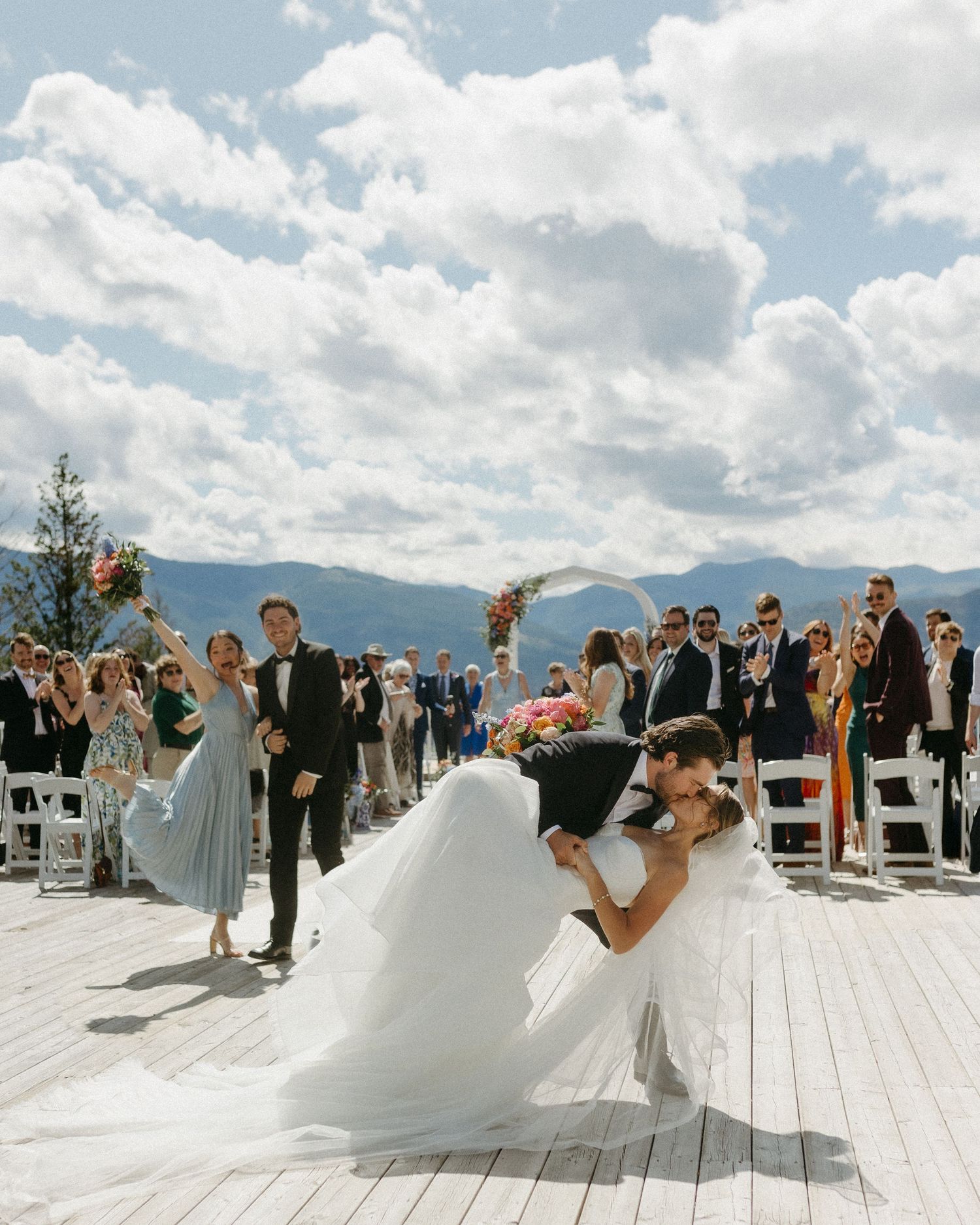 Wedding couple performing romantic dip on outdoor deck with mountain views.