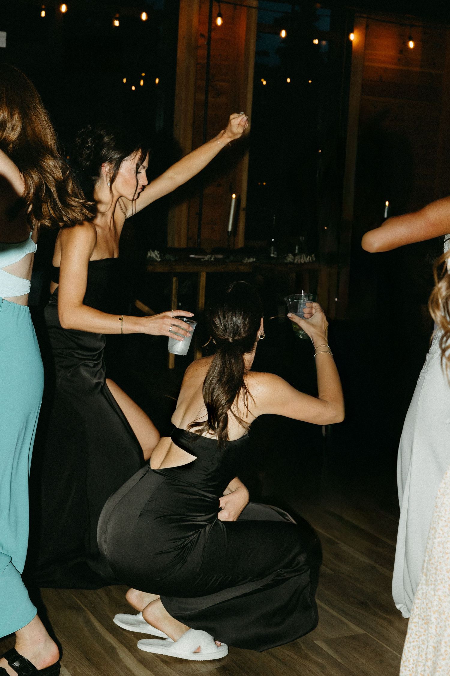 Wedding guests dancing on wooden floor during evening reception.