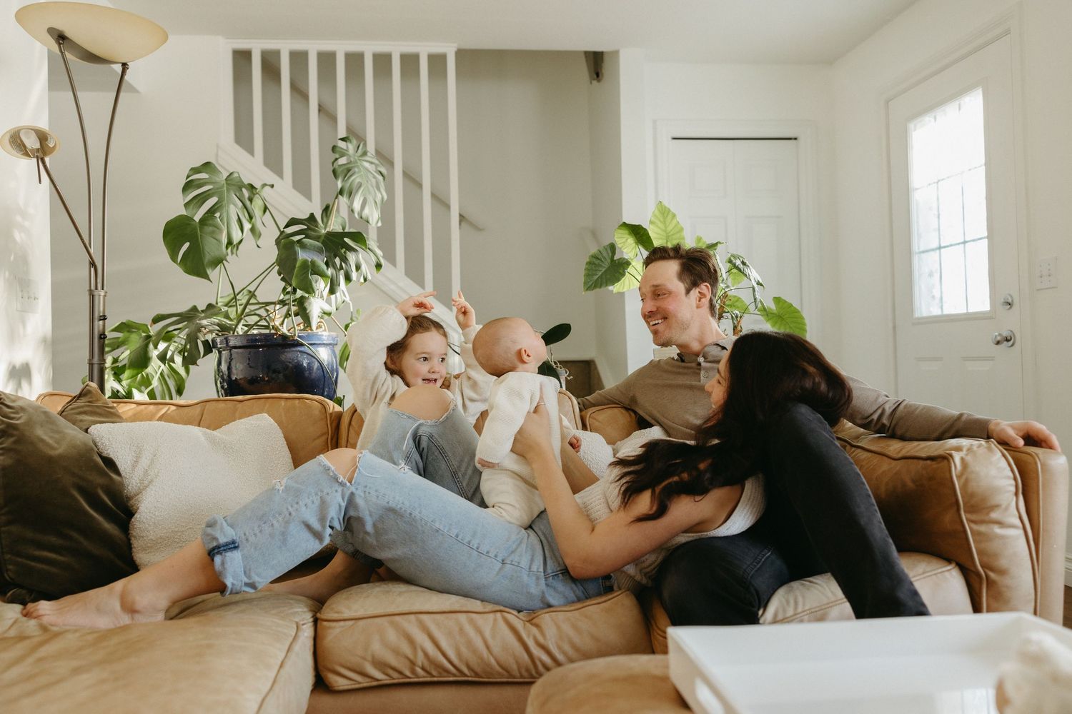 A family shares tender moments together on a tan couch in a sunlit living room.