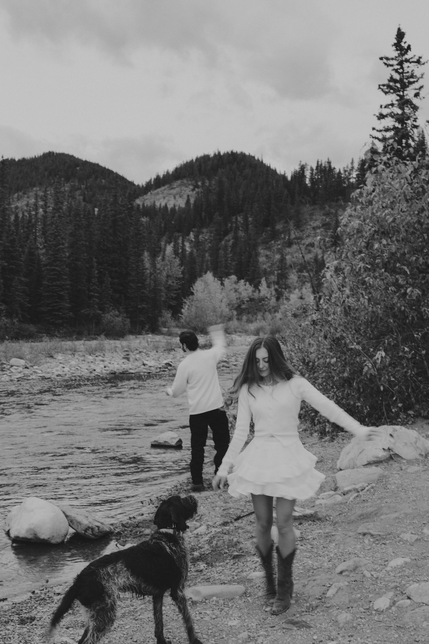 A couple walks with their dog along a scenic mountain lake.