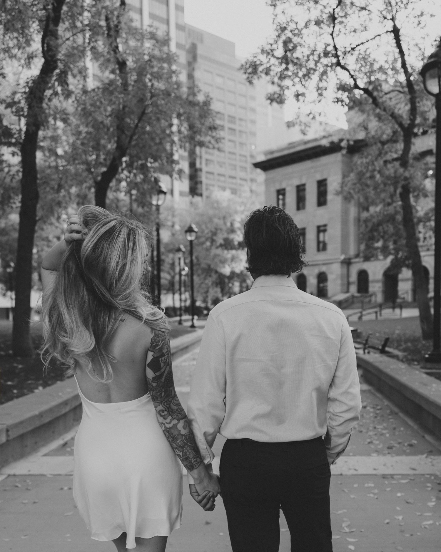 Couple walks hand in hand down a tree-lined urban street on an autumn day.