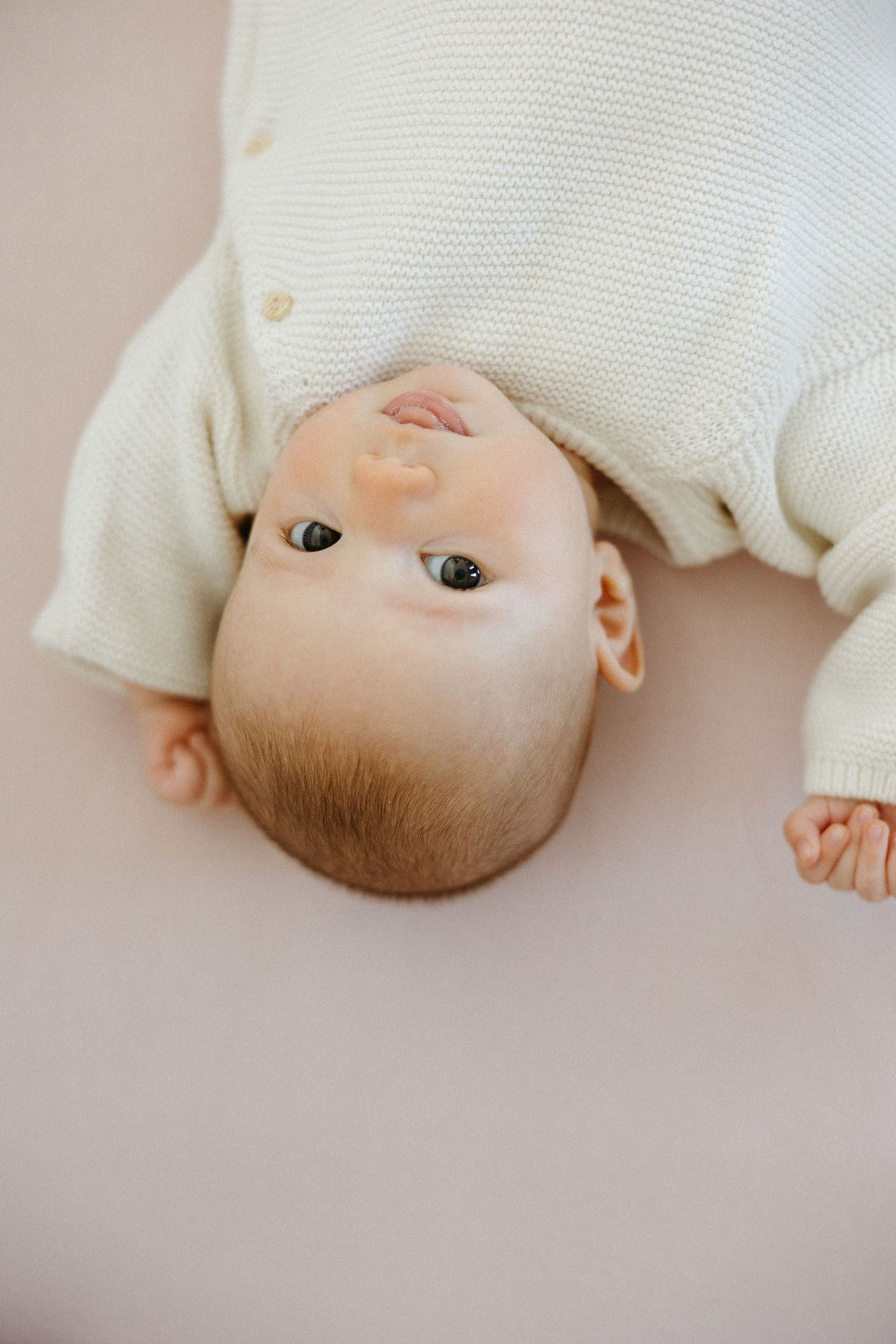 Close-up portrait of a baby in white clothing lying on a light colored background.