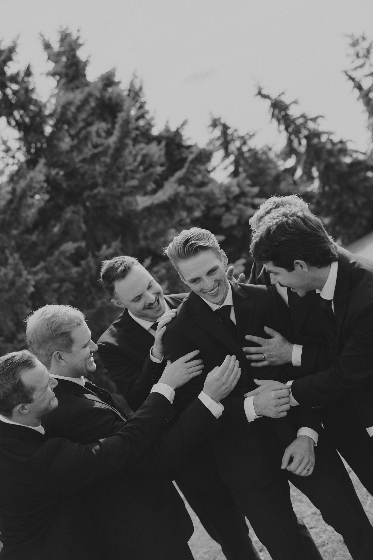 Groomsmen in black suits sharing a candid moment outdoors.
