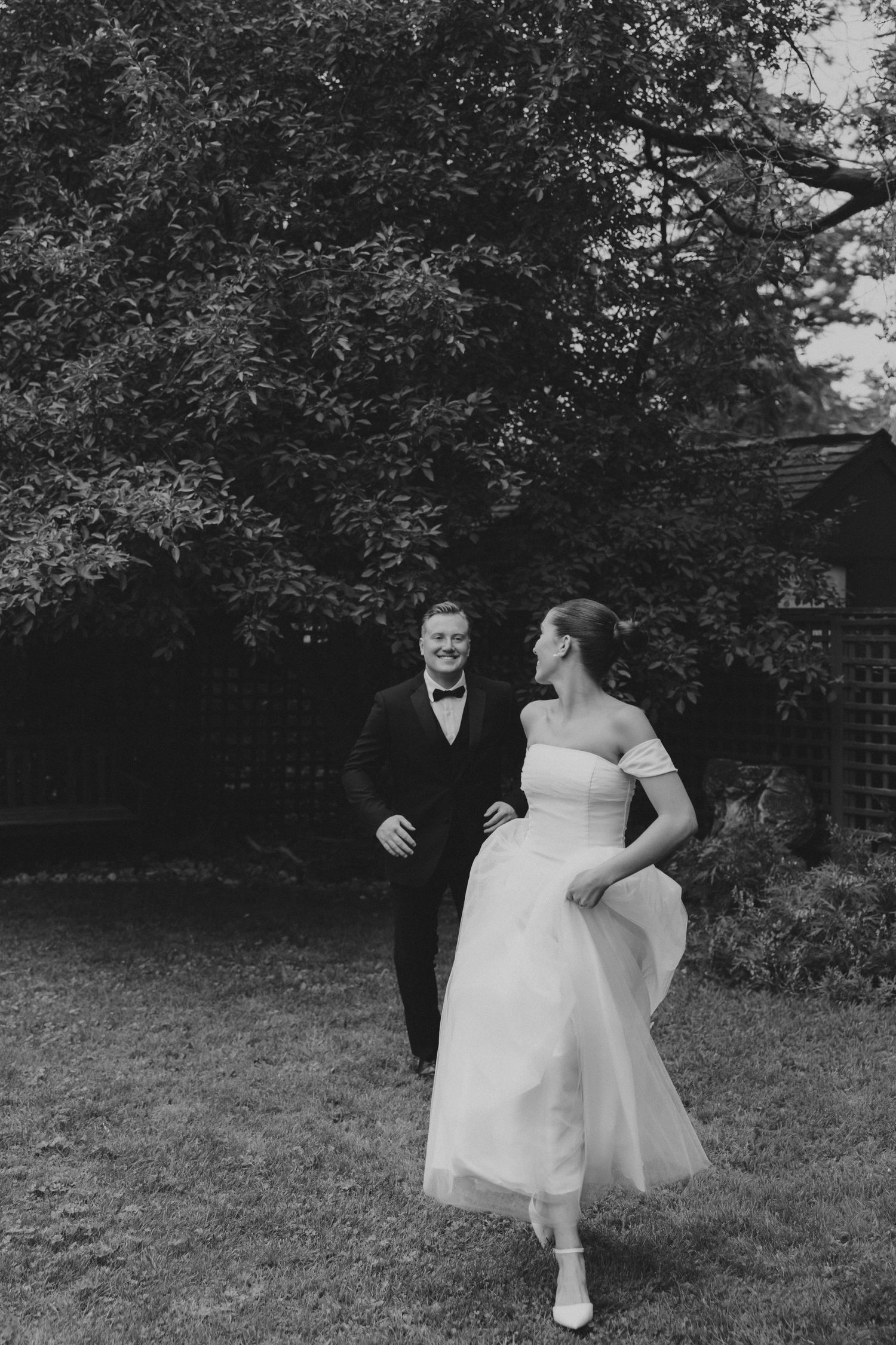 A couple dances playfully in a garden setting with trees in the background.