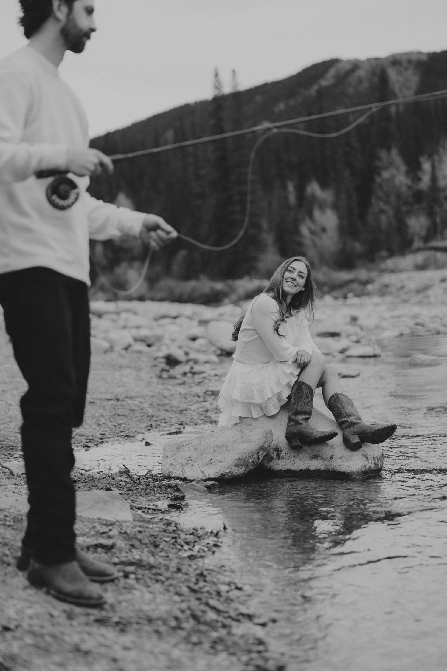 Black and white photo of a couple enjoying a playful moment by a river.