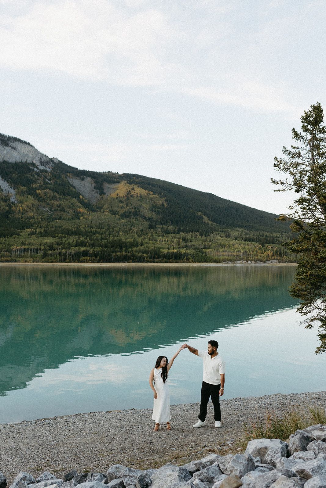 Scenic mountain lake view with rocky shore and turquoise waters under cloudy skies.