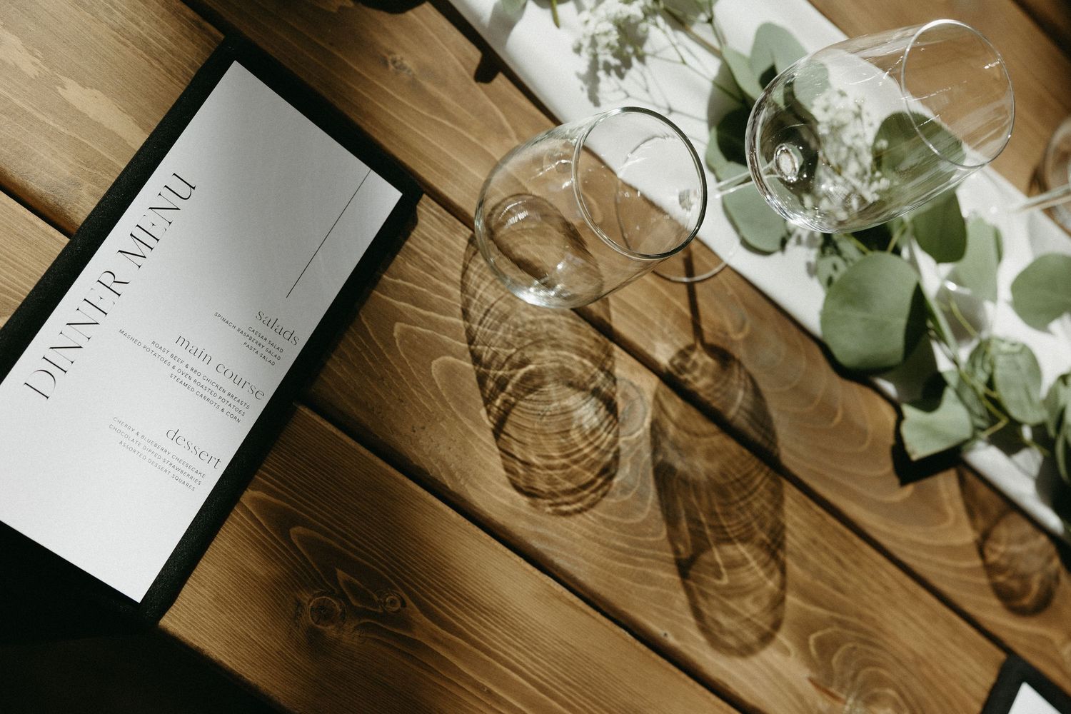 Wedding reception table details with wine glasses and menus on rustic wooden surface.
