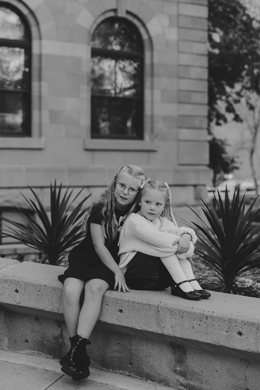Vintage black and white photo of children sitting on a stone ledge outside a building.
