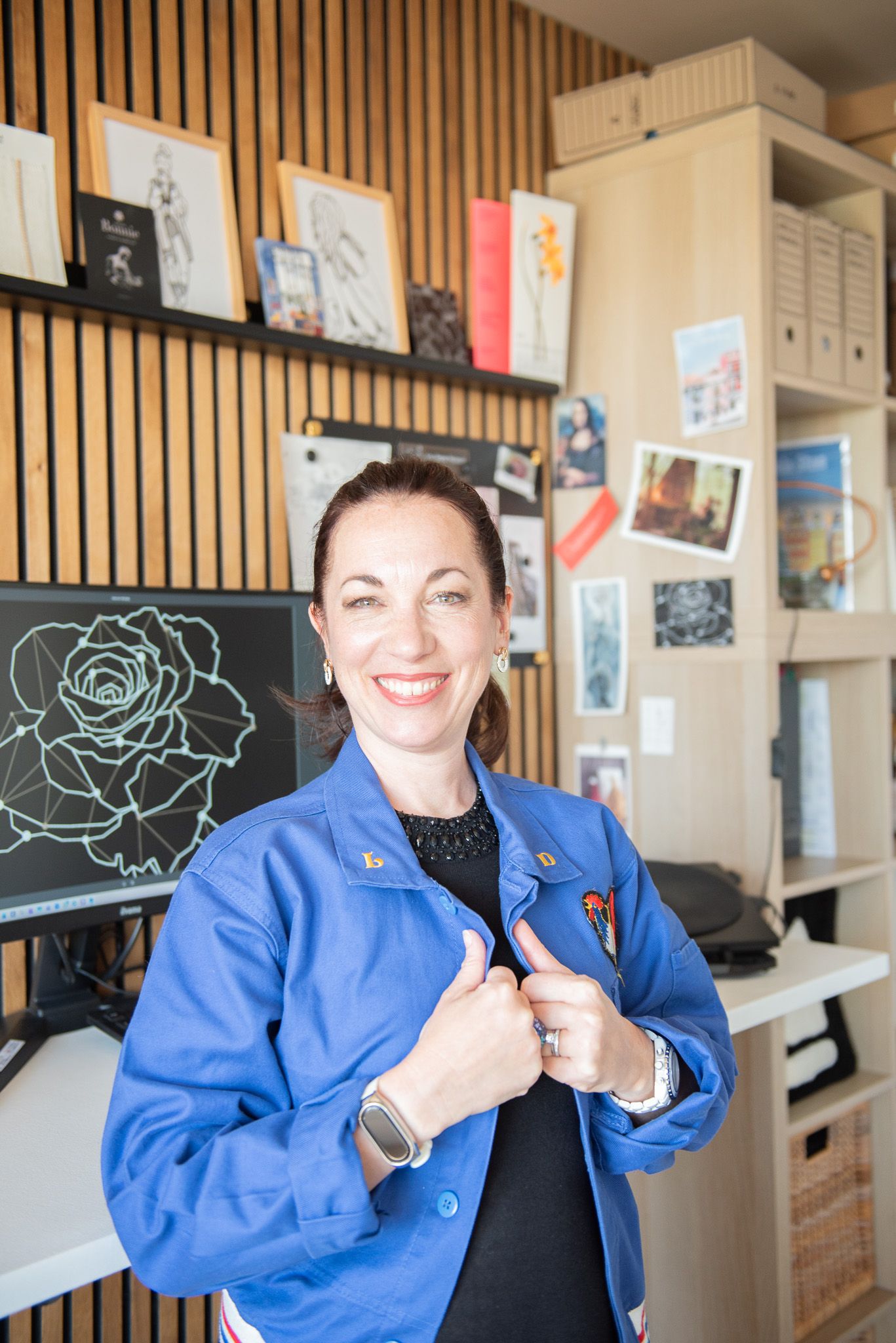 Lise, vêtue d'une veste bleue, lors de son shooting de branding dans son studio de design, avec des illustrations
