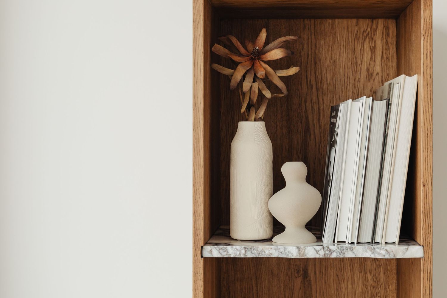 Étagère en bois avec des vases en céramique blanche, une fleur séchée et des livres blancs empilés.