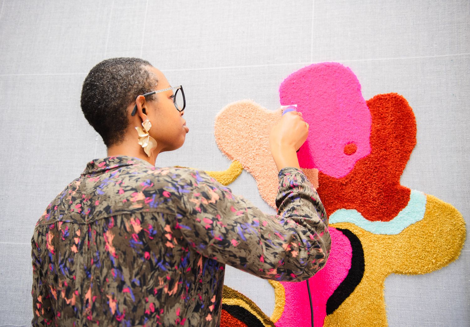 Artist working on colorful abstract floral textile wall art with pink and yellow shapes.