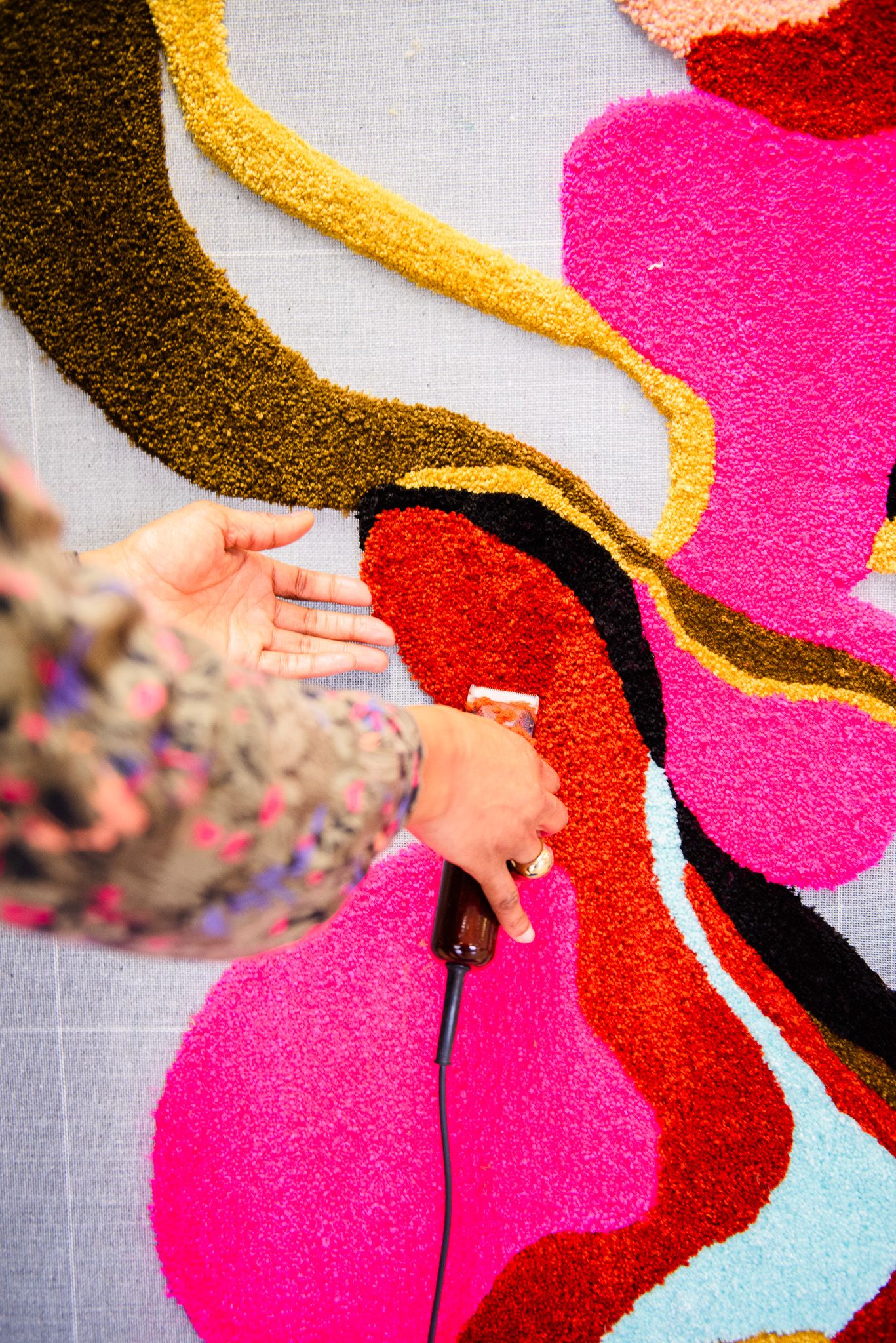 Overhead view of artist tufting colorful abstract rug with pink, red, yellow and black yarn design.