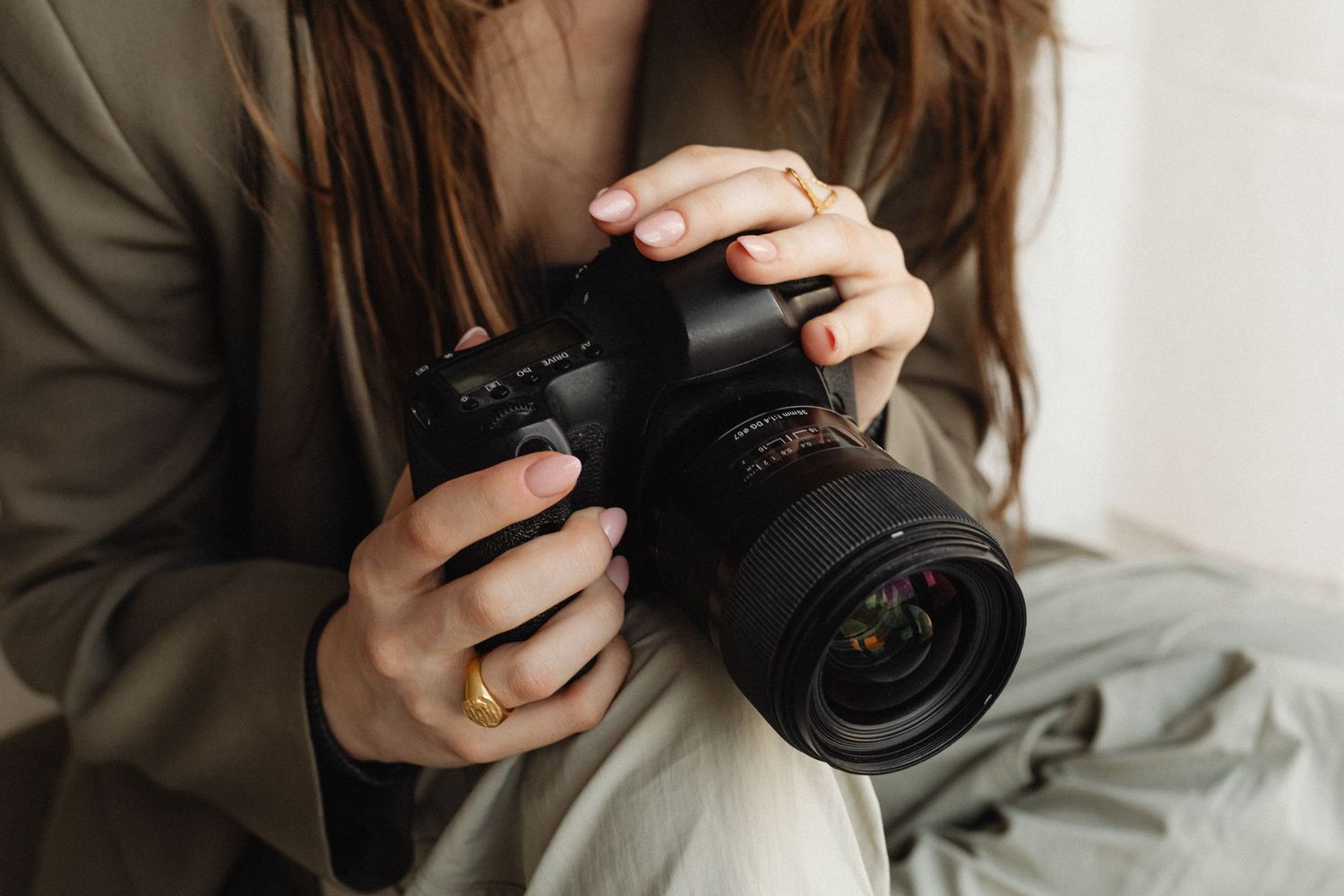 Woman in gray blazer holding professional DSLR camera with large lens in her hands.