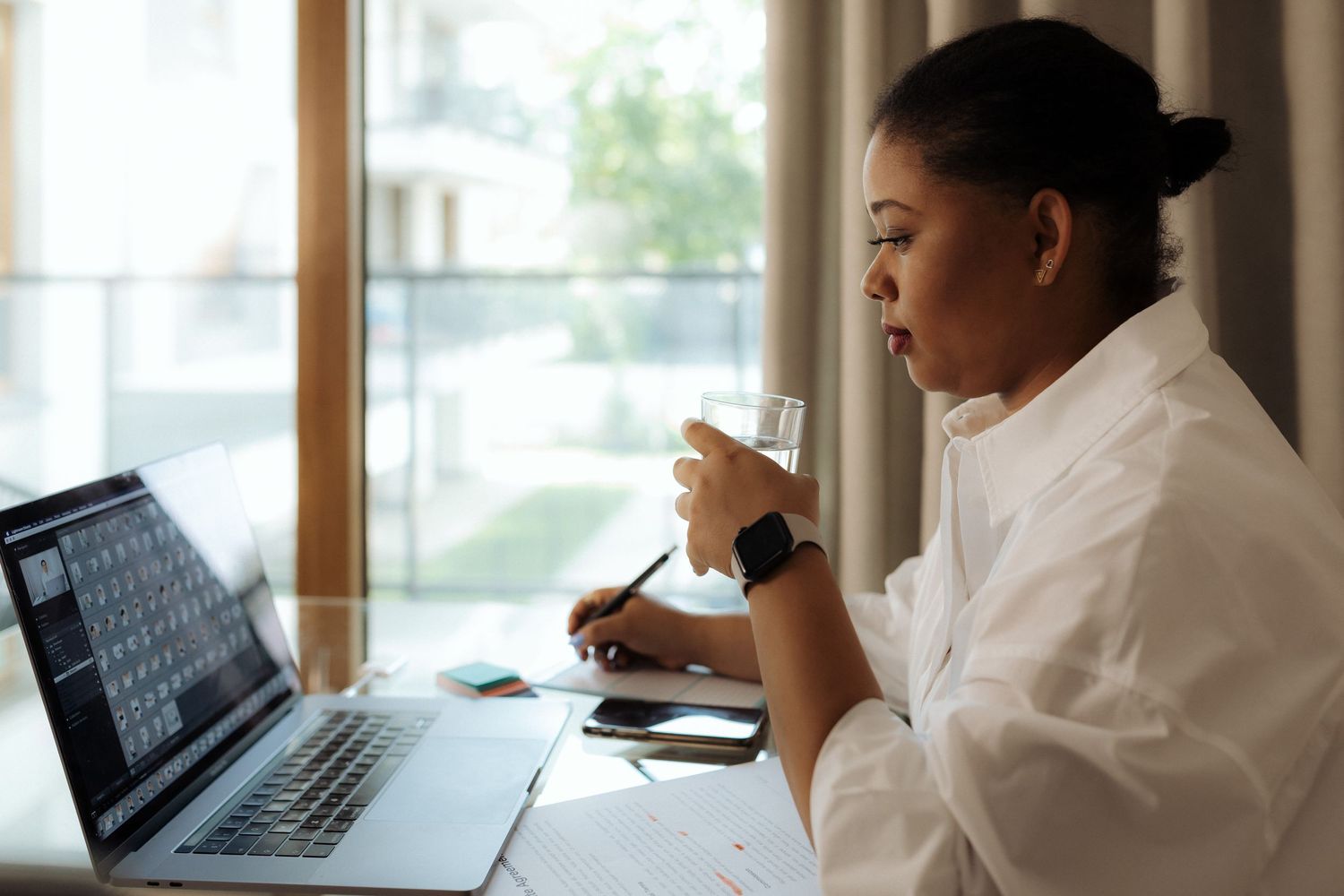 Woman drinking water while working on laptop at desk.
